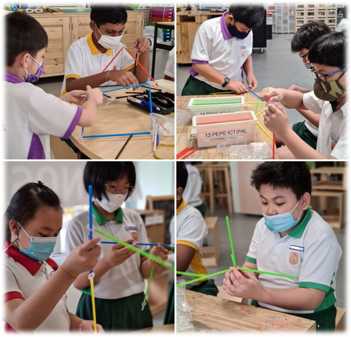 Four school children wearing masks build structures using colorful straws at wooden tables in a classroom.