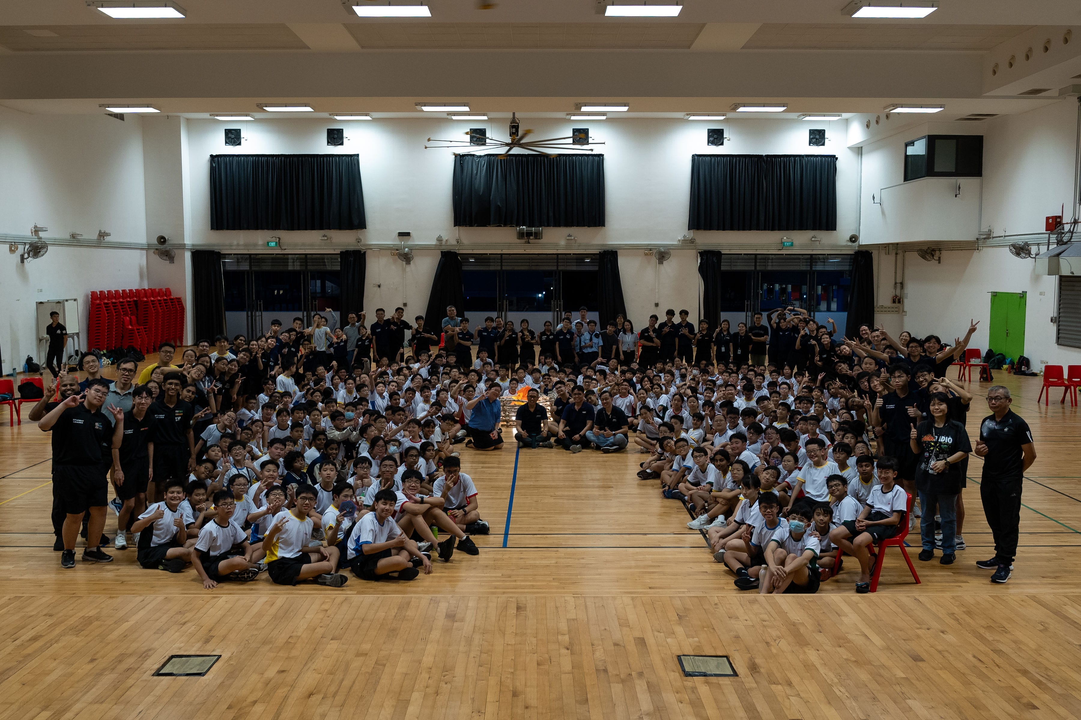 Large group of students in white shirts and adults in black shirts posing together in a school gymnasium.