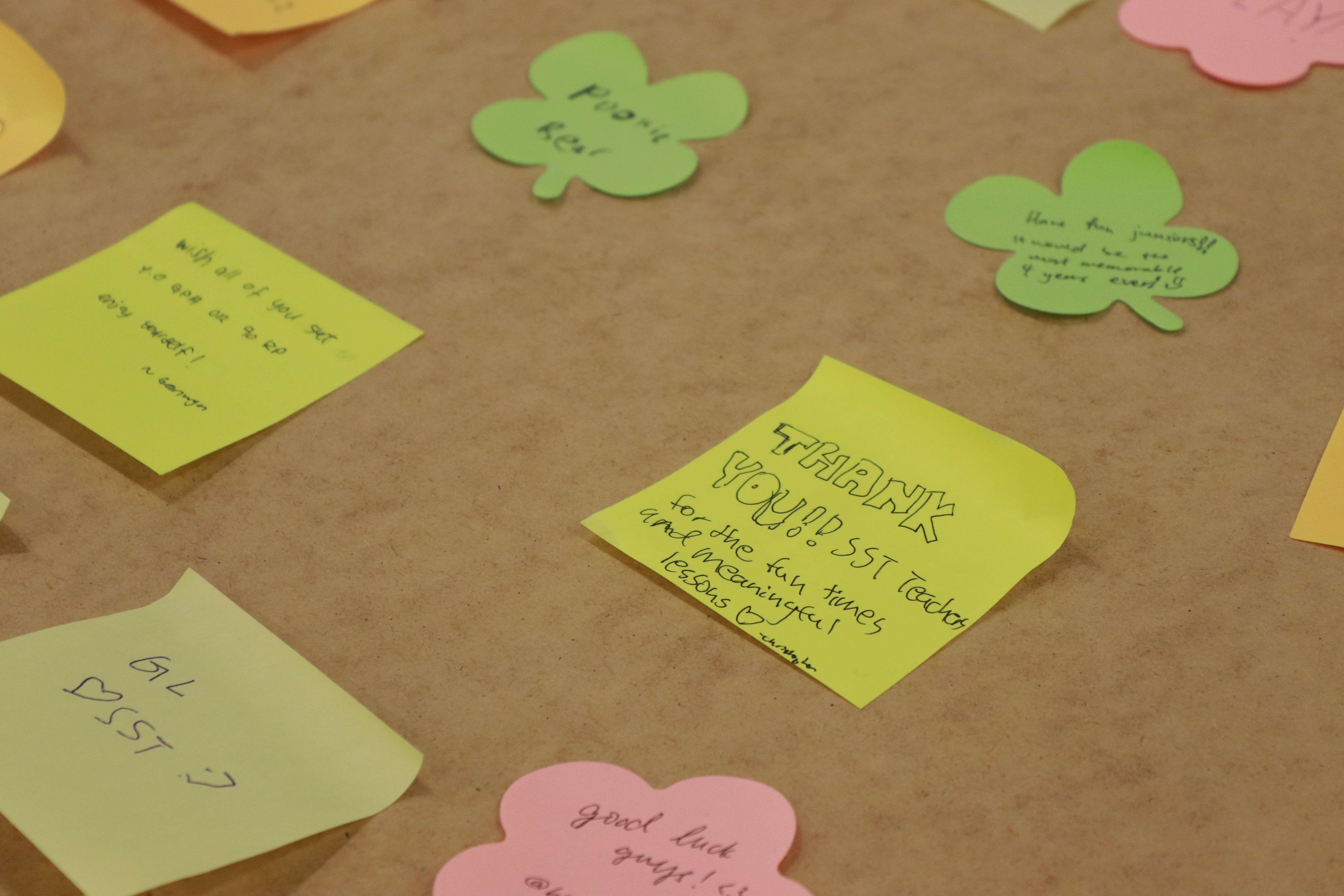 Yellow sticky notes and green shamrock cutouts with handwritten thank-you messages pinned to a brown board.