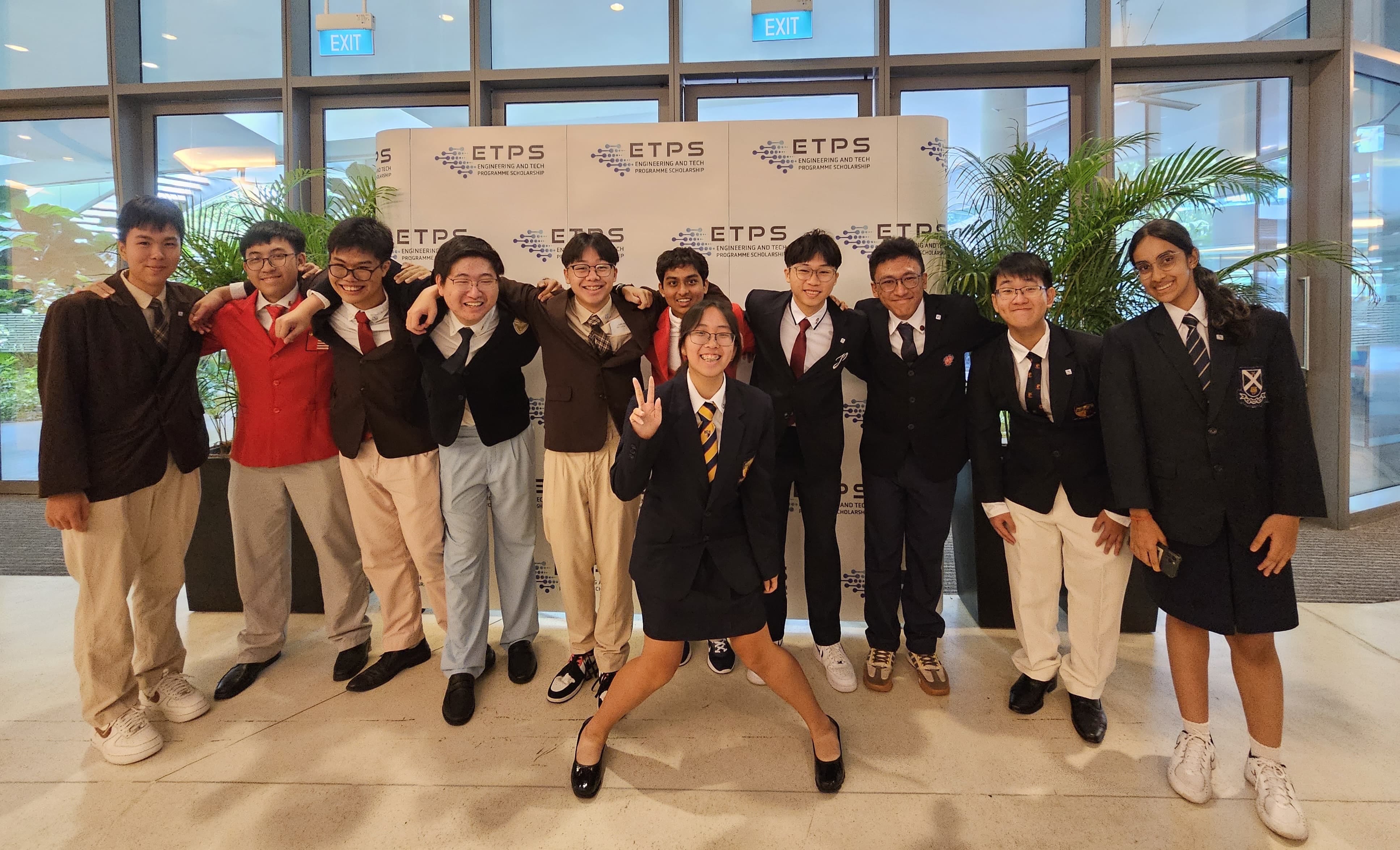 A group of smiling students in school uniforms pose in front of an ETPS scholarship event backdrop.
