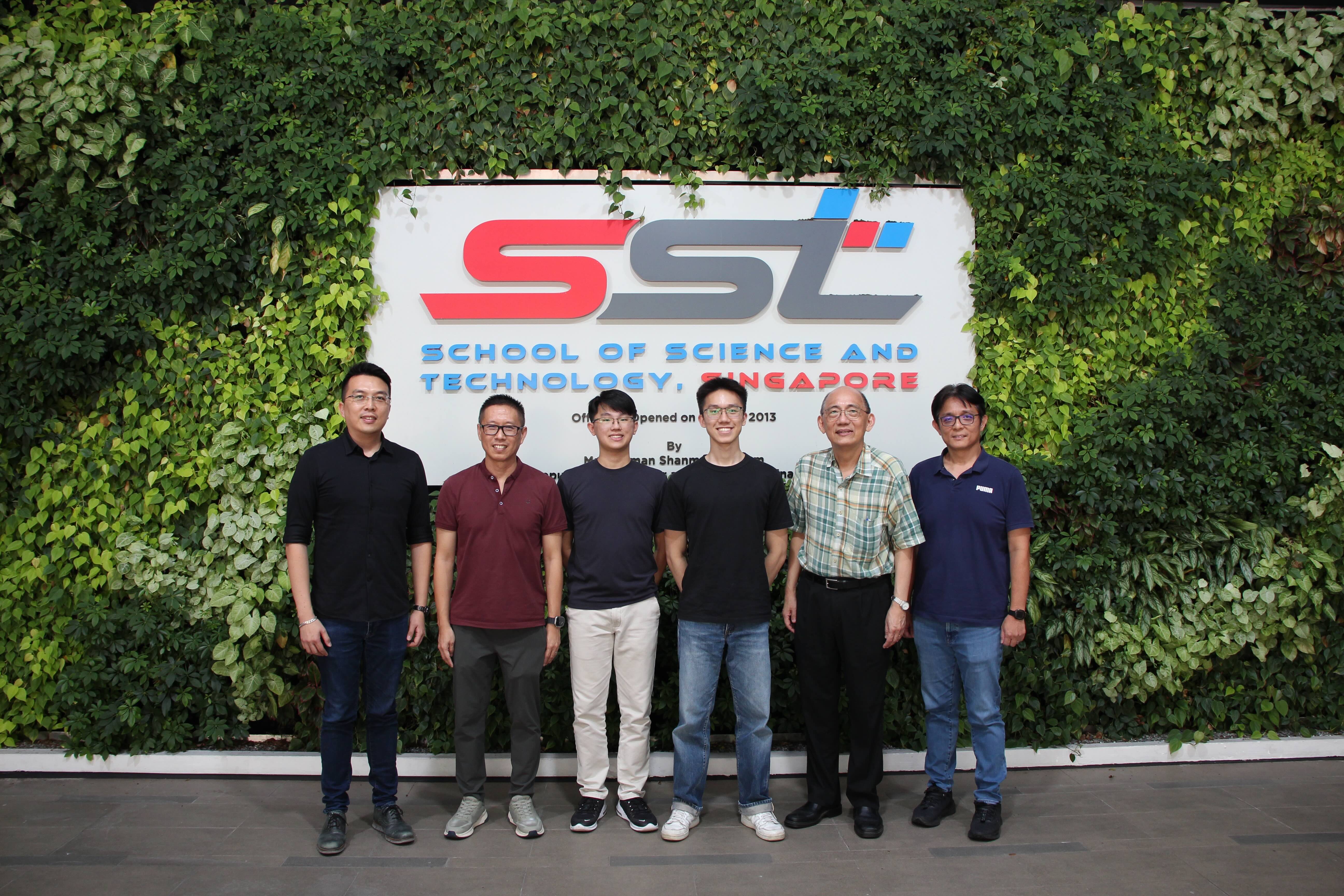 Six people pose in front of the School of Science and Technology Singapore sign on a green plant wall.