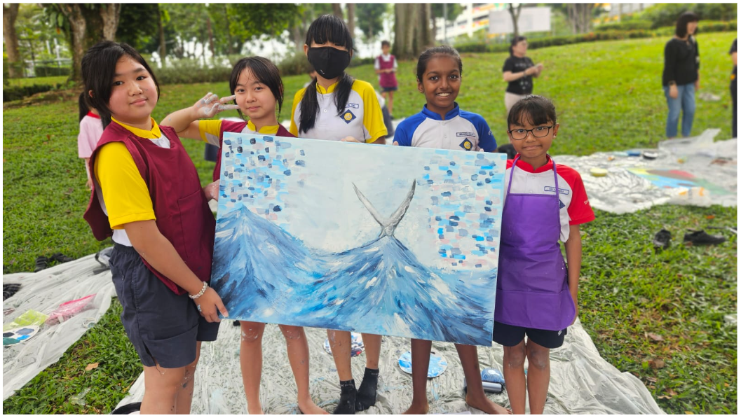 Five children in school uniforms stand outdoors holding a blue ocean wave painting on a grass field.