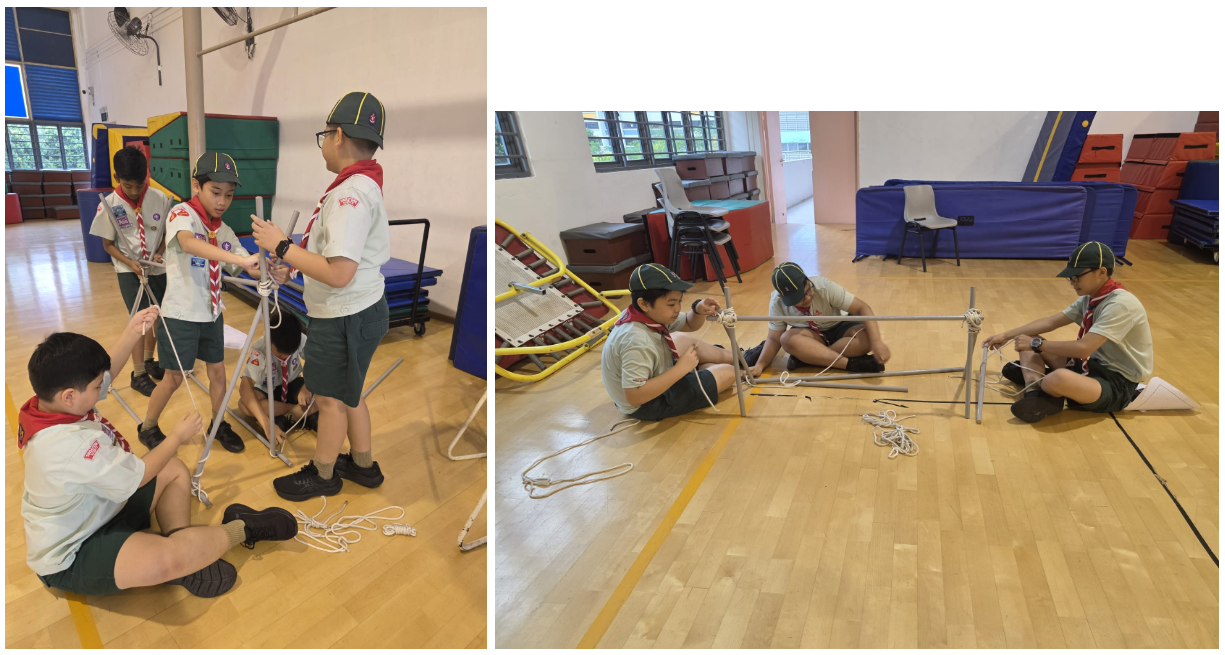 Boy scouts in uniform tying ropes around metal poles to build a structure on an indoor gym floor.