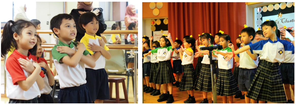 Young schoolchildren in uniforms participate in a performance, some clapping and gesturing on a decorated stage.