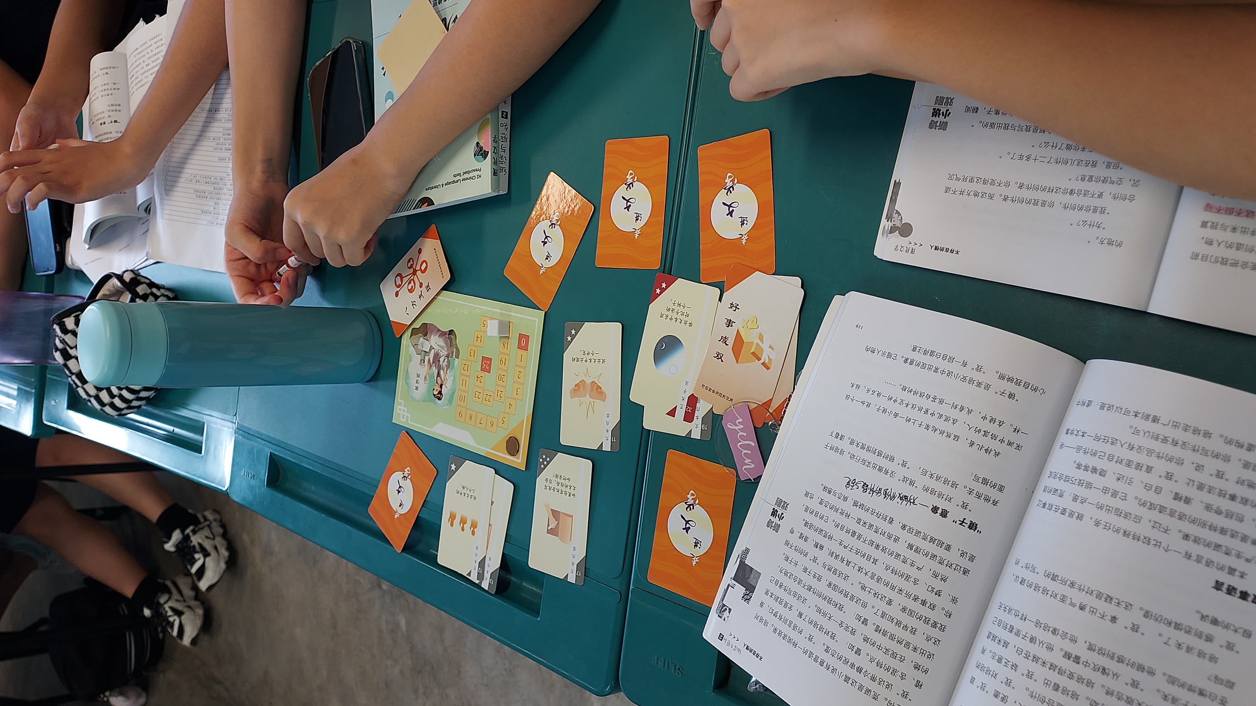 Students sit around a desk engaged in a Chinese card game.