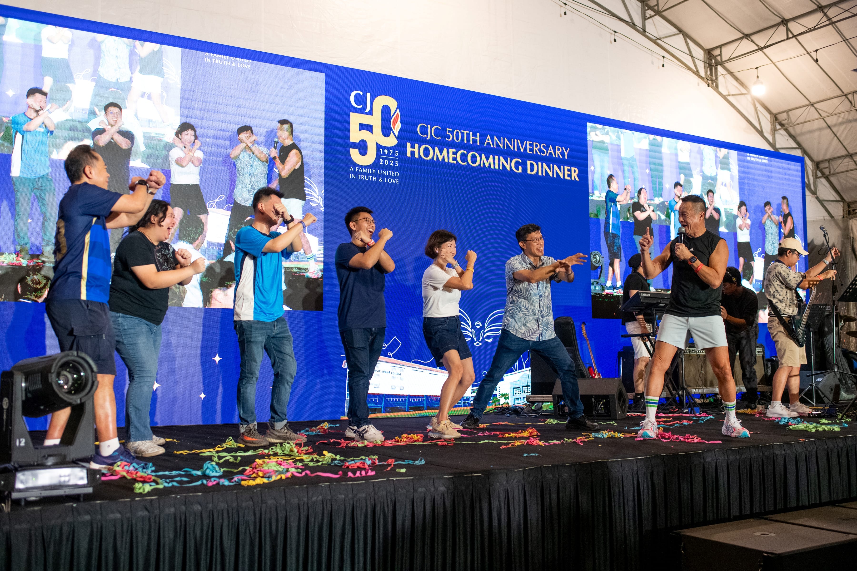 People on stage mimic dance moves as a man with microphone leads, with a CJ 50th anniversary backdrop.