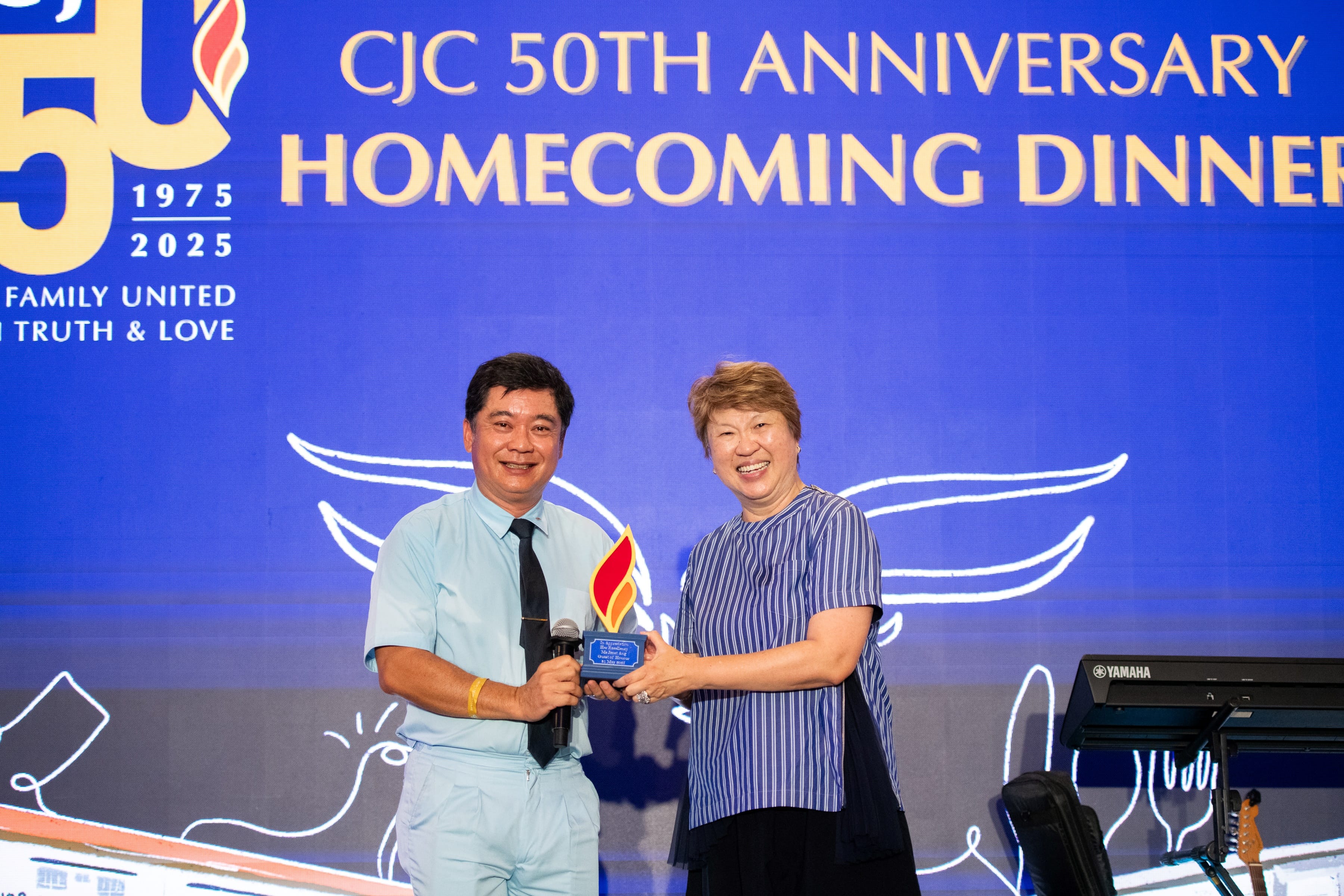 Two people smile holding an award onstage under text reading CJC 50th Anniversary Homecoming Dinner.