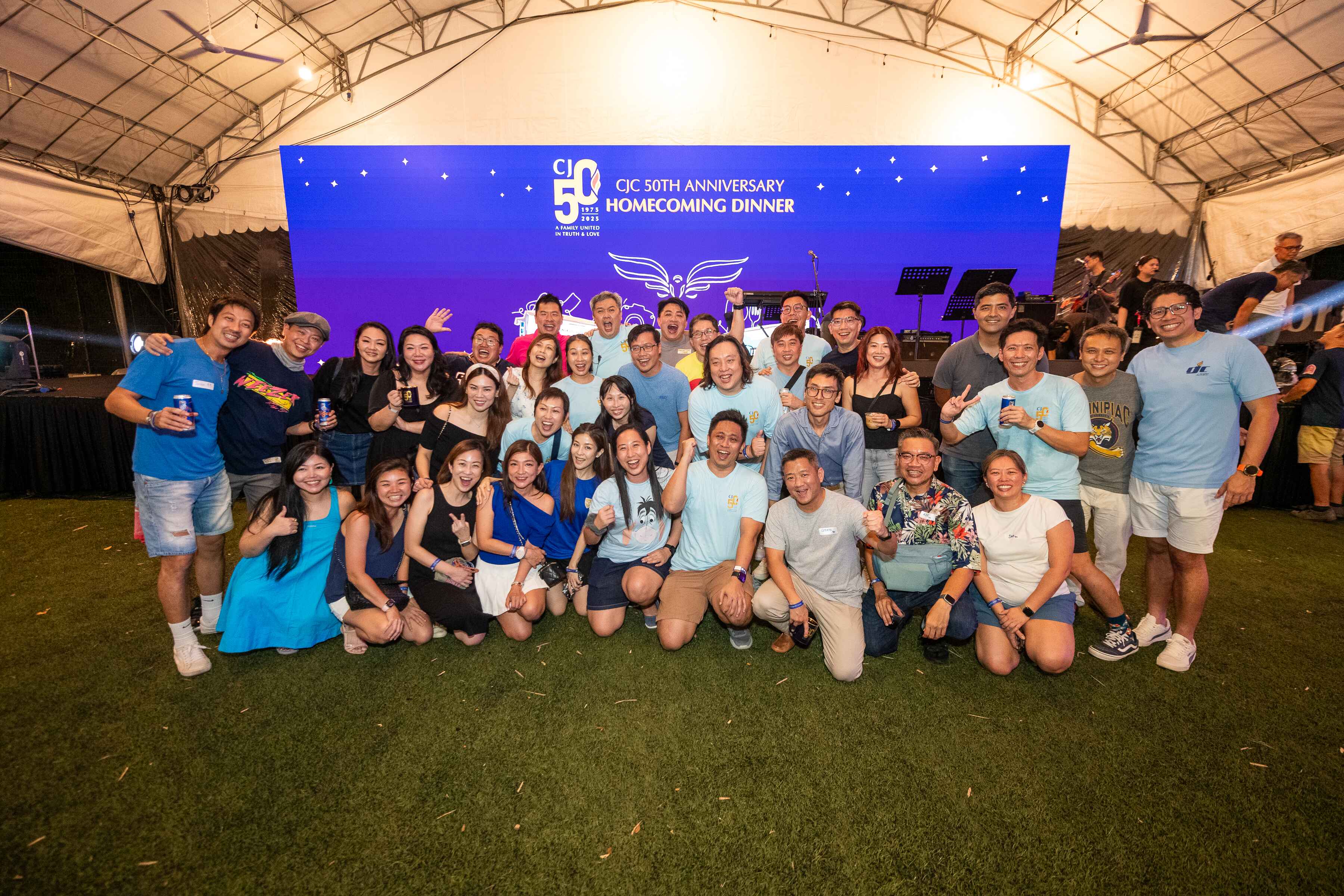 Large group of smiling people posing in front of a blue banner reading CJC 50th Anniversary Homecoming Dinner.