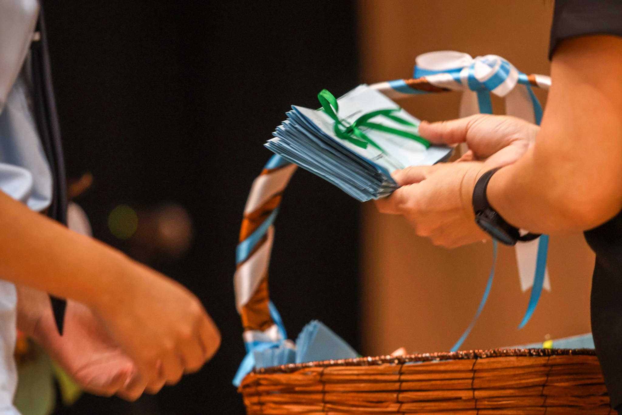 A person hands a stack of blue envelopes tied with green ribbon over a wicker basket decorated with blue ribbons.