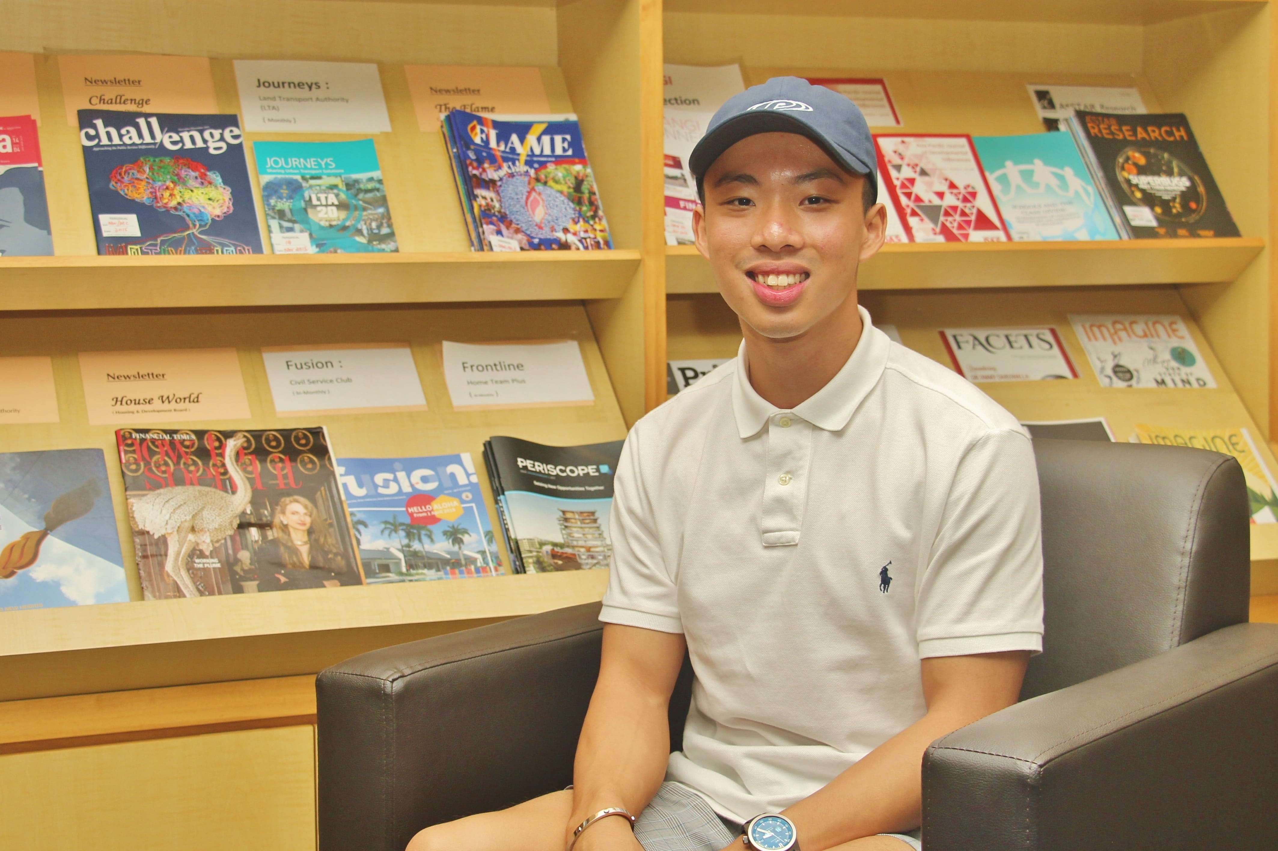 Smiling man in a cap and white polo sits in an armchair in front of shelves of magazines.