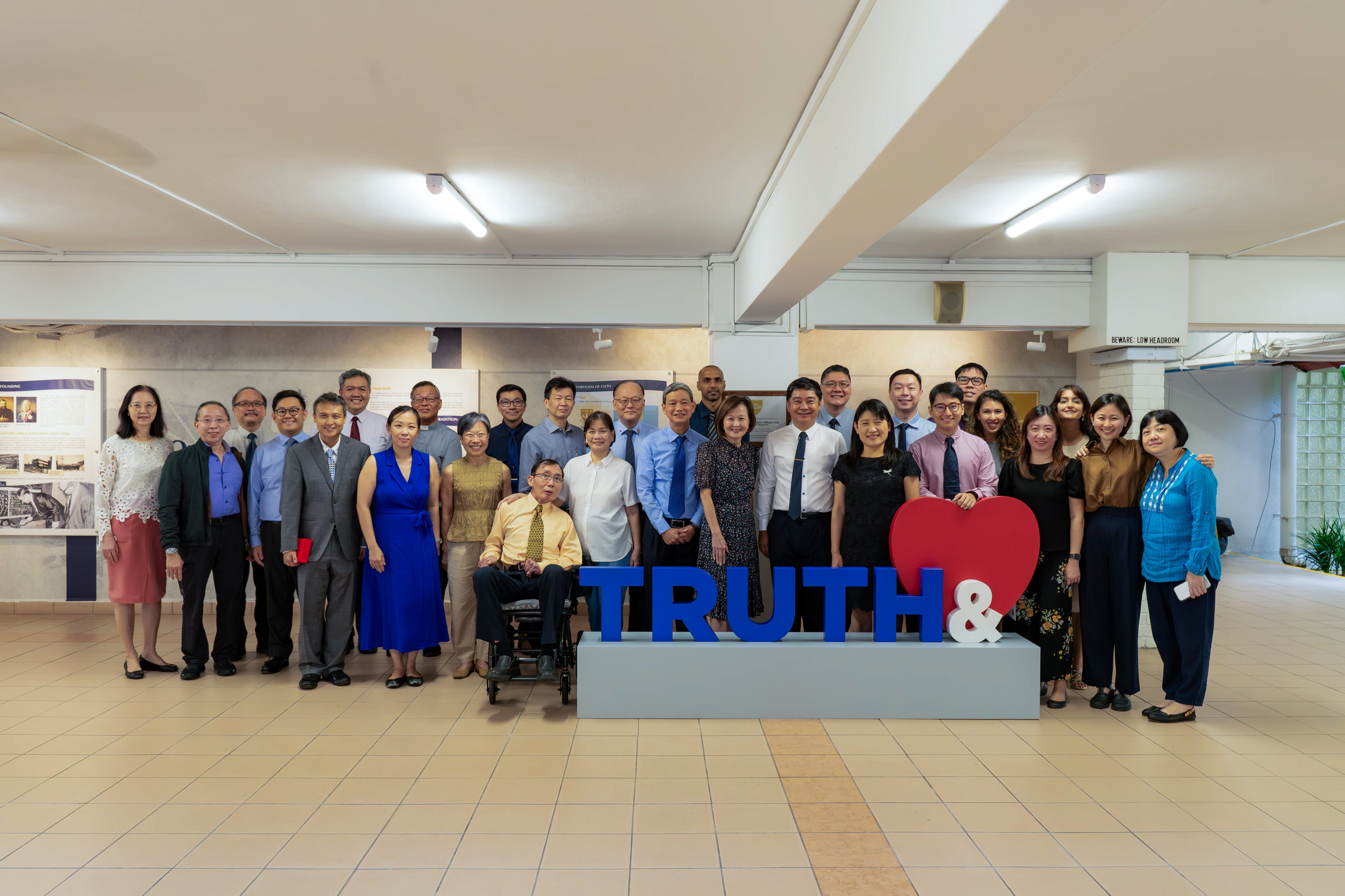A large group of people posing indoors behind a sign reading TRUTH& with a red heart beside it.