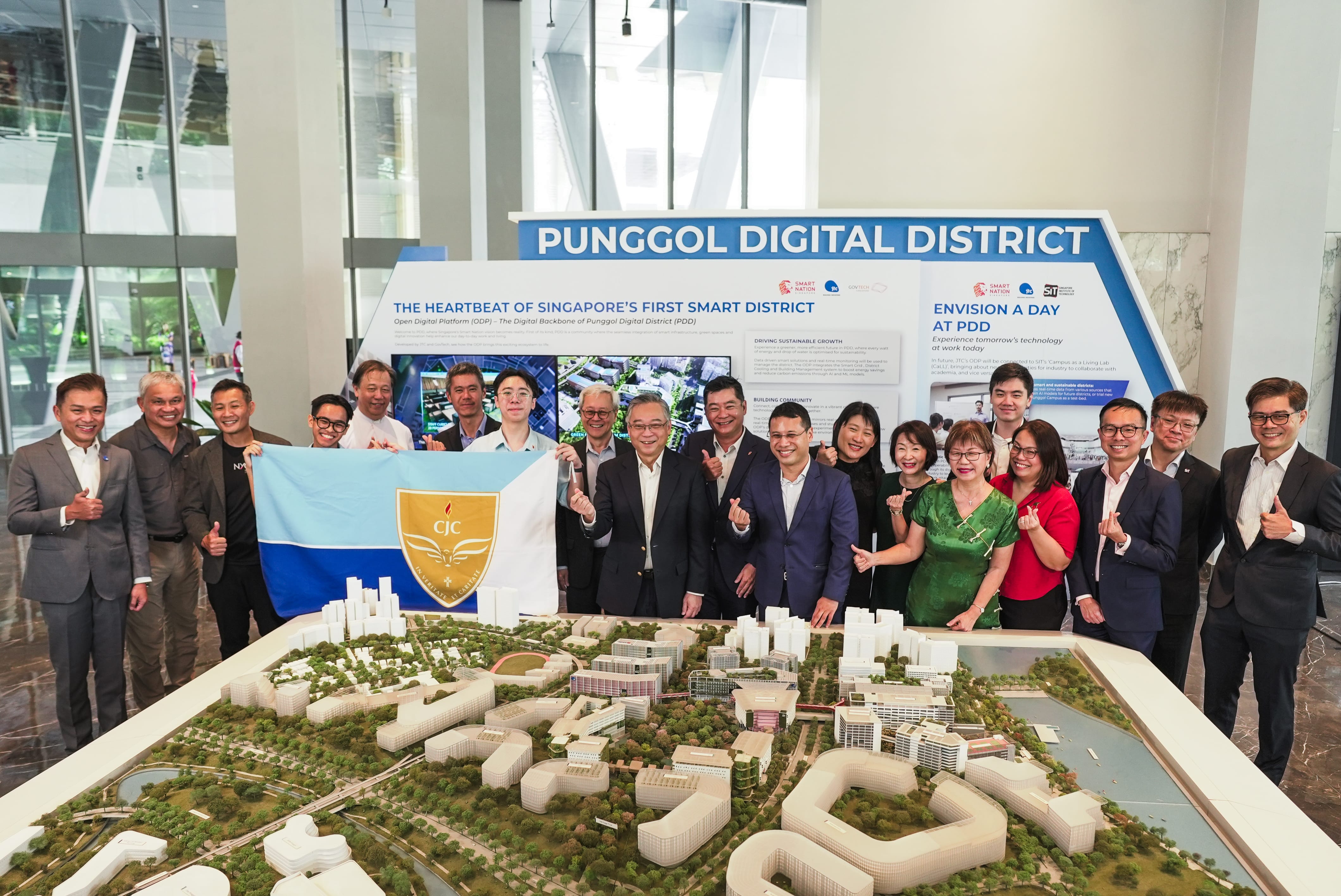 Group posing behind a city model, holding a flag, under a Punggol Digital District display sign.