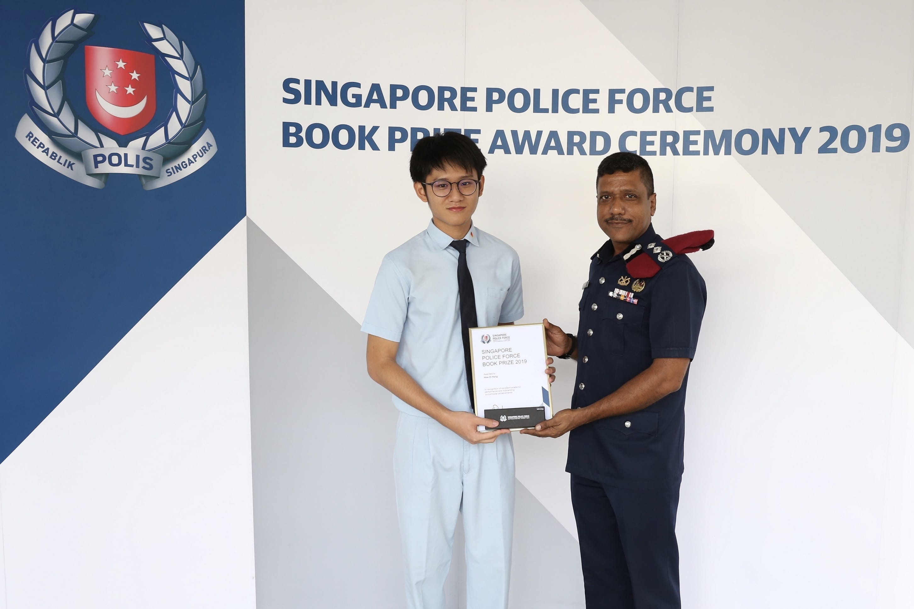 A young man and a police officer hold a certificate at the Singapore Police Force Book Prize Award Ceremony 2019.