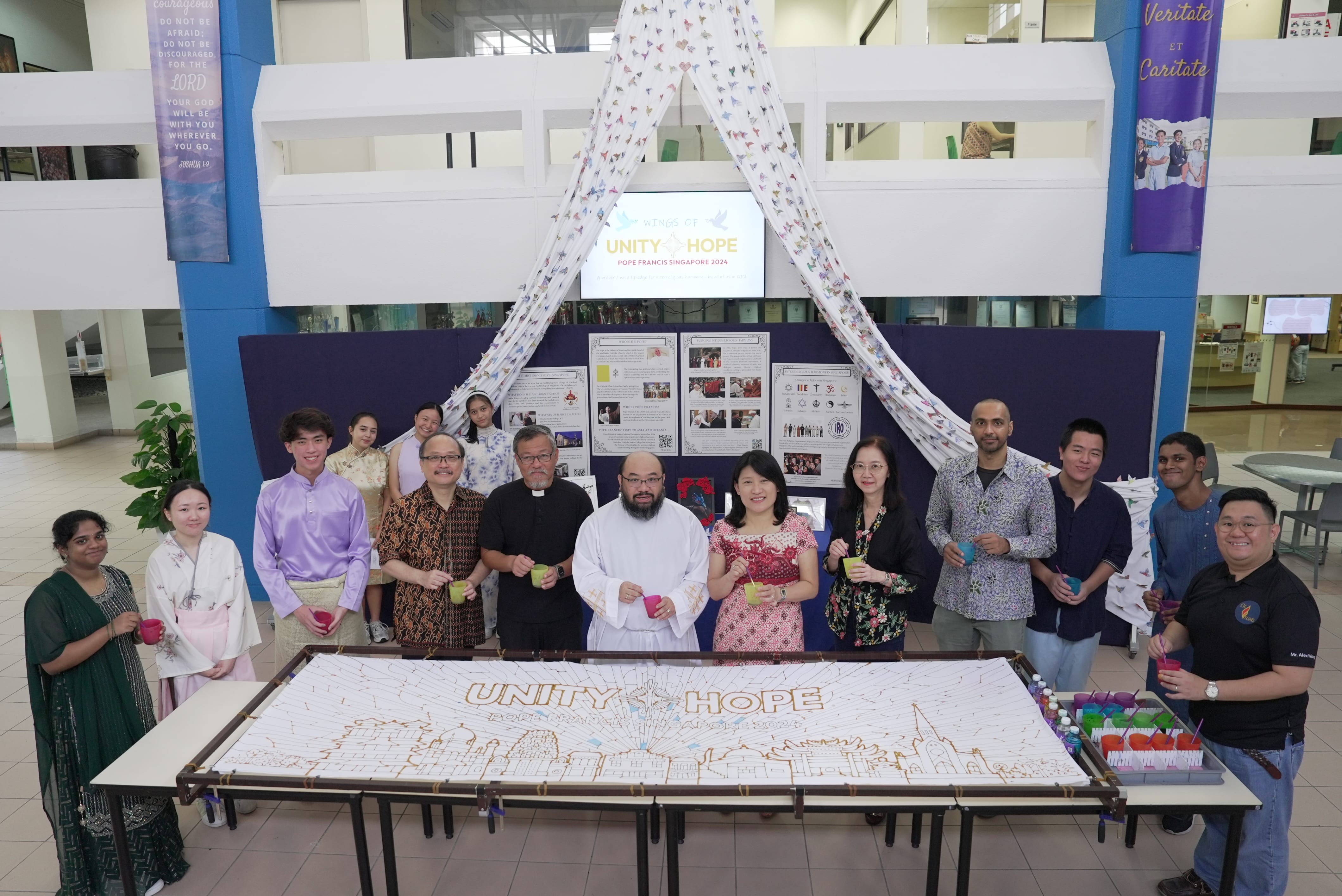 Group of 12 posing behind long UNITY HOPE banner on table, holding cups; draped cloth overhead.
