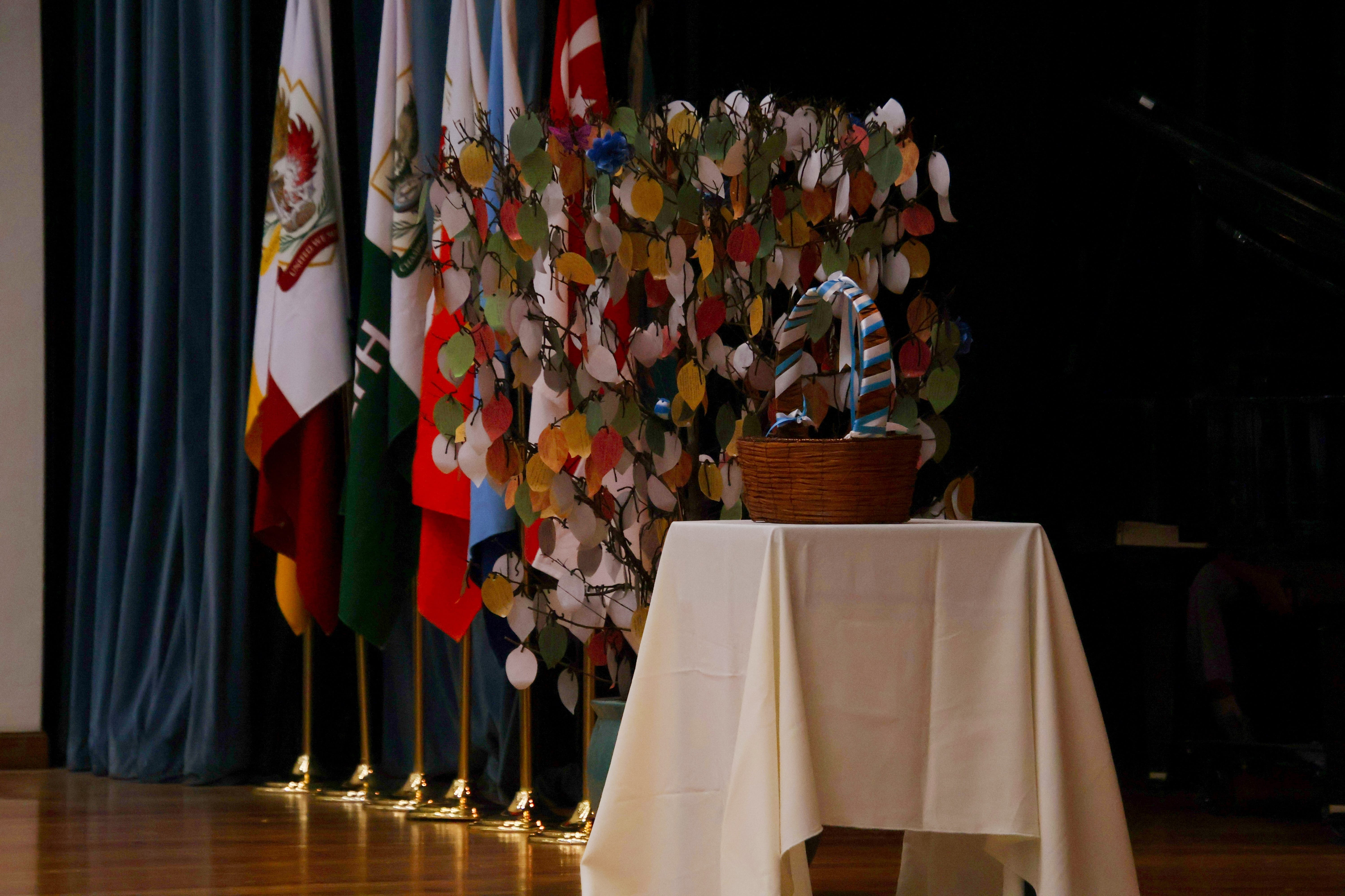 Wicker basket on a draped table beside a tree with colorful paper leaves and flags in the background.