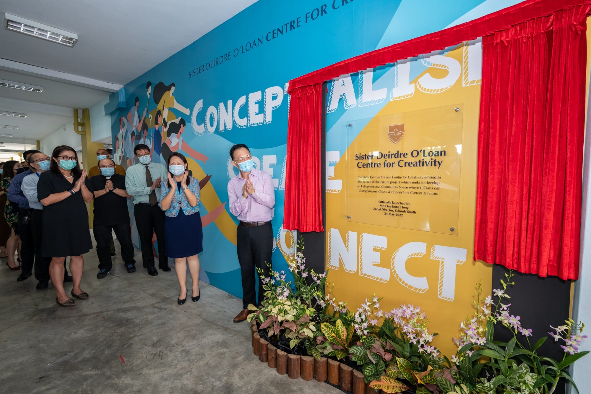 People wearing masks applaud at the unveiling of the Sister Deirdre O'Loan Centre for Creativity plaque.
