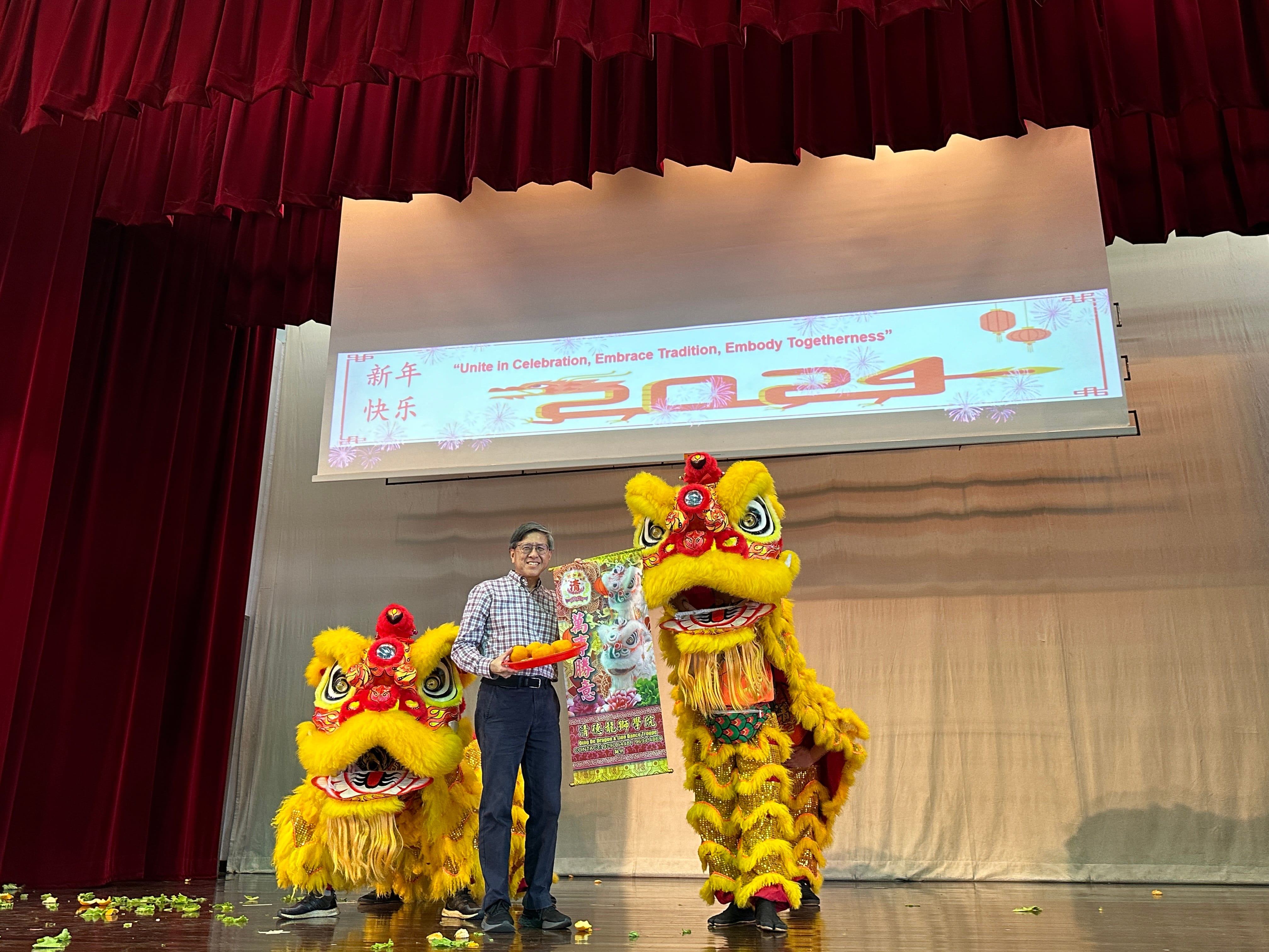 A man stands on stage between two yellow lion dance costumes at a 2024 Chinese New Year celebration event.