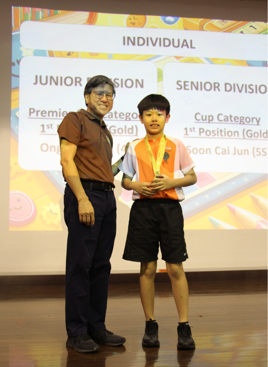 A man and a young boy wearing a gold medal pose in front of a screen showing Junior and Senior Division awards.