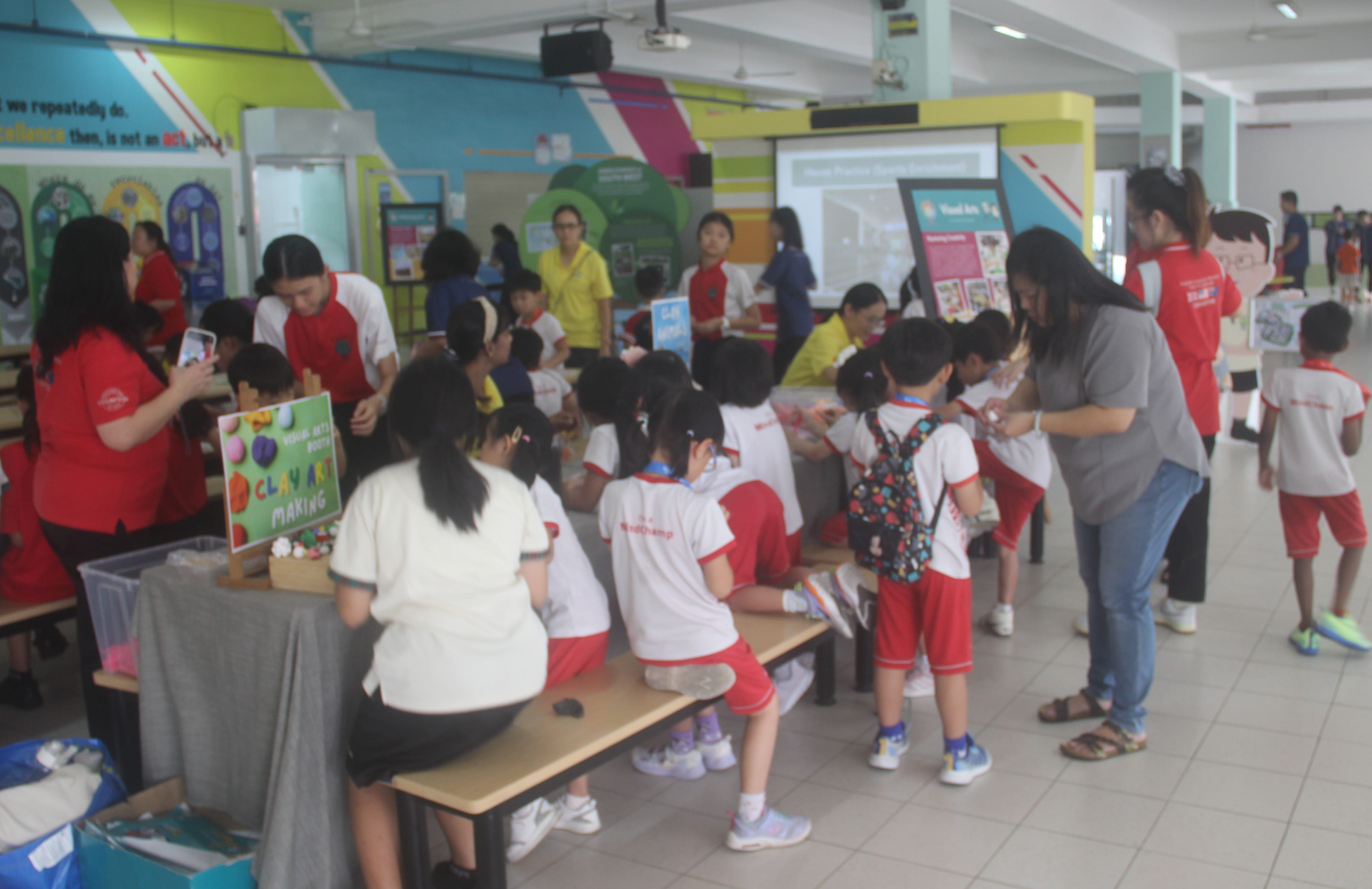 Children in school uniforms participate in a clay art making activity at a colorful indoor school event.
