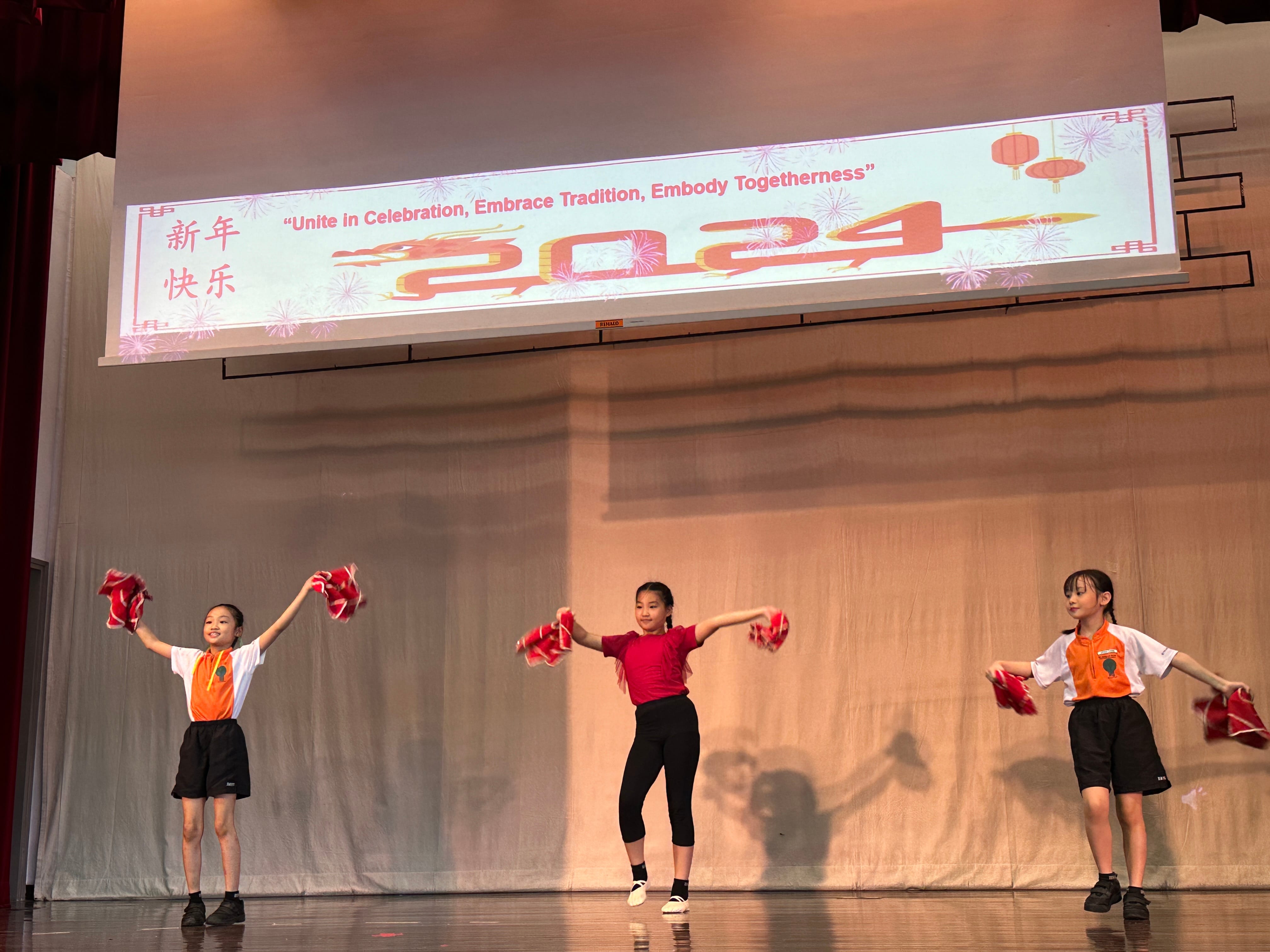 Three girls dance on stage with red props at a 2024 Chinese New Year celebration event.
