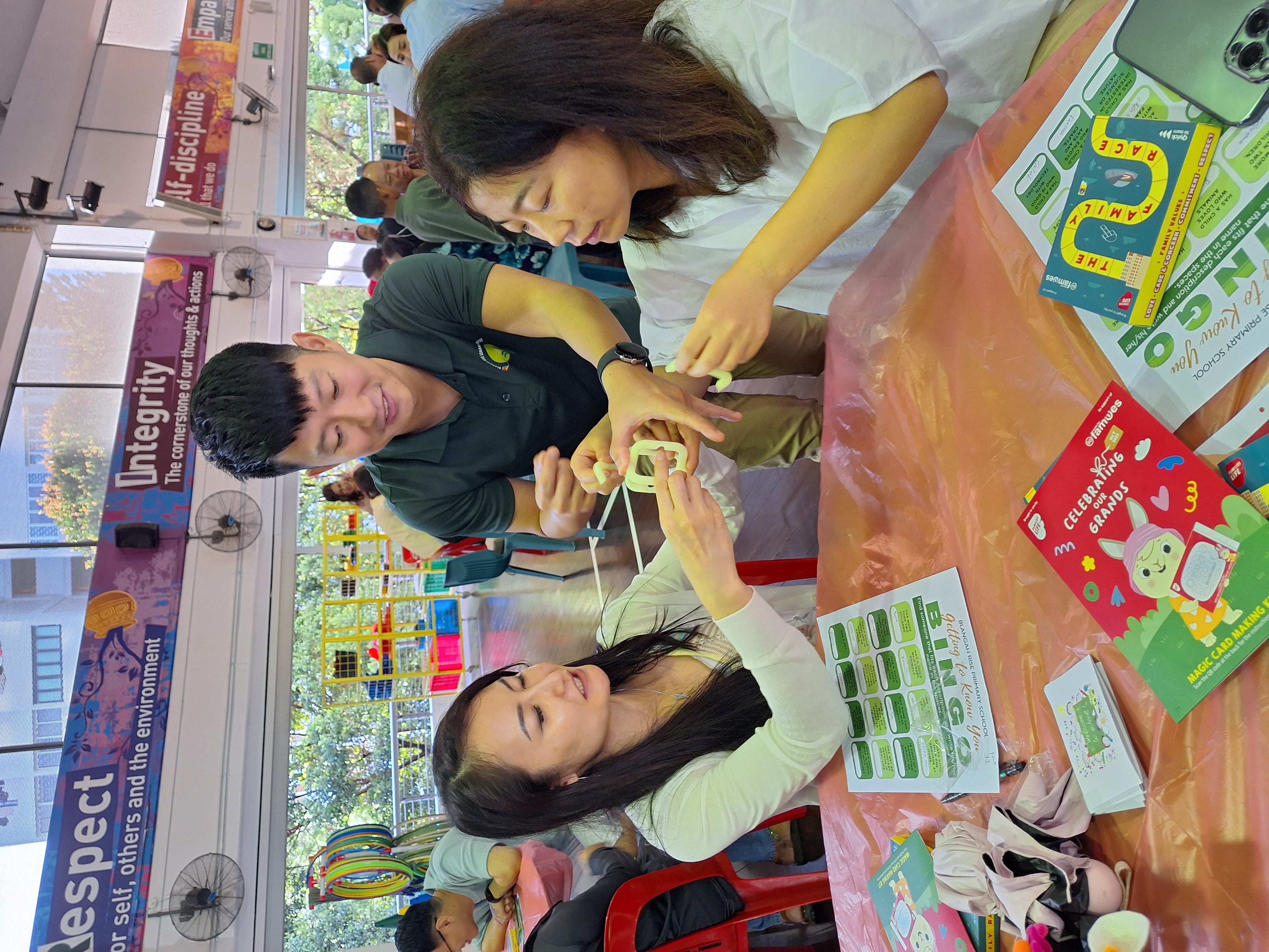 Three people at a table work together on a craft with string, surrounded by colorful cards and games.