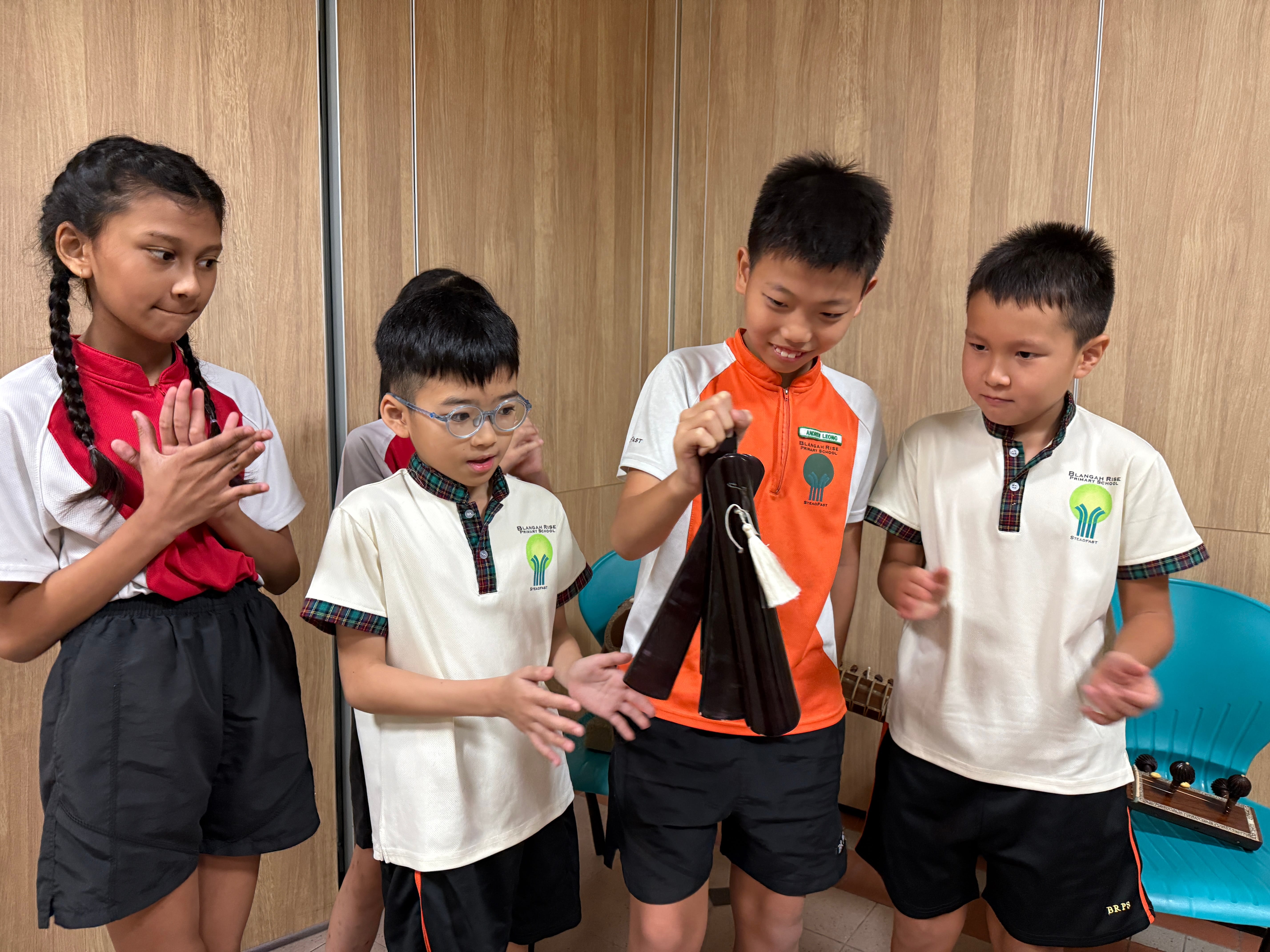 Four children in school uniforms watch a boy holding a dark object with a white tassel.