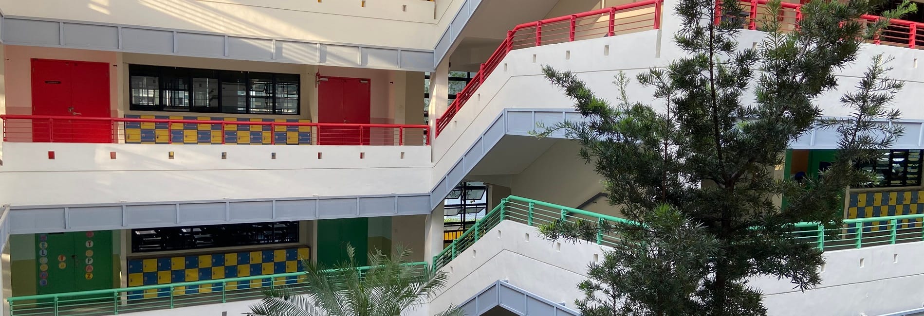 Multi-story school building interior courtyard with colorful lockers, red railings, and trees growing inside.