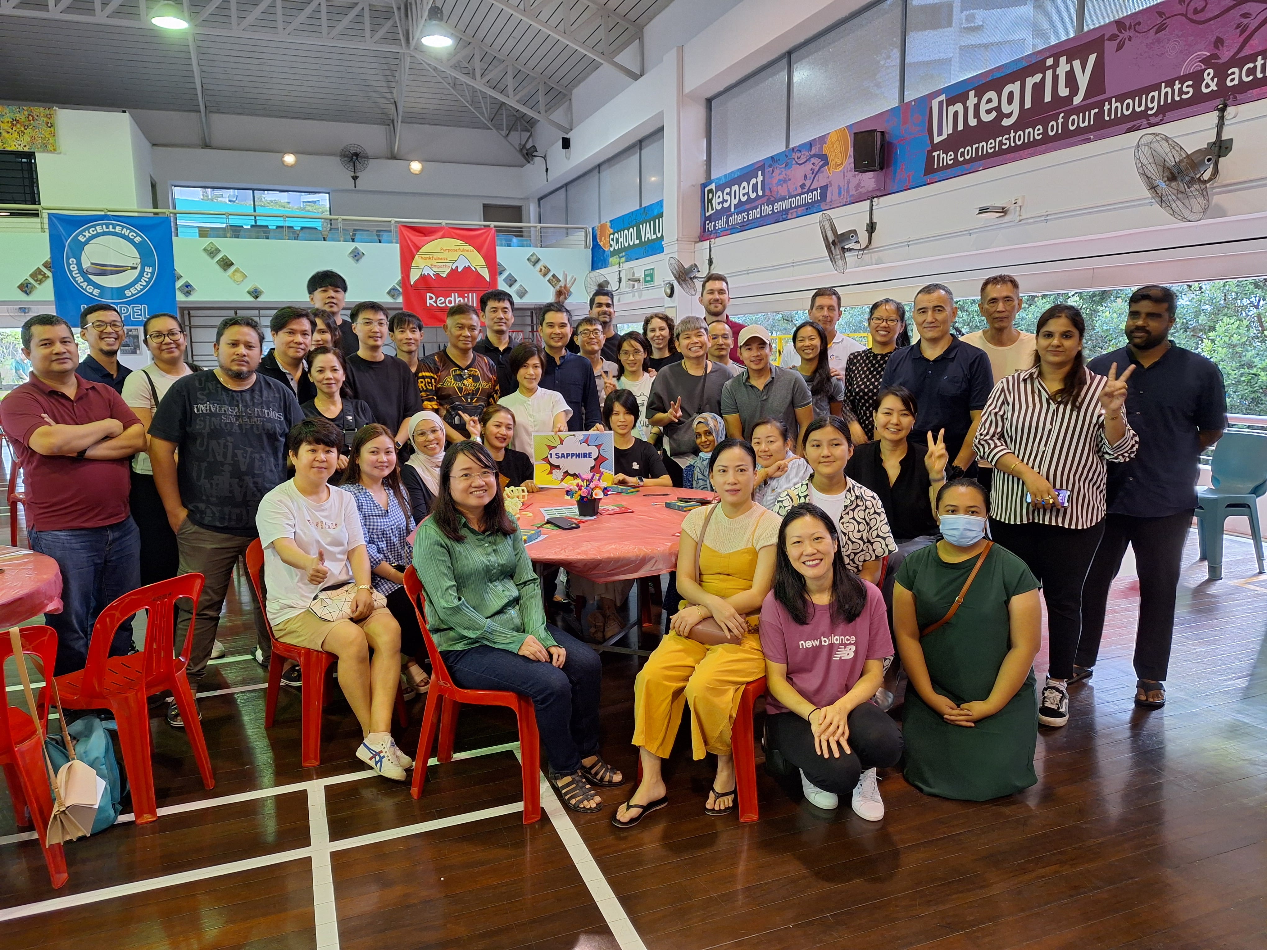 Large group gathered around tables in a hall, posing for a photo under Respect and Integrity banners.