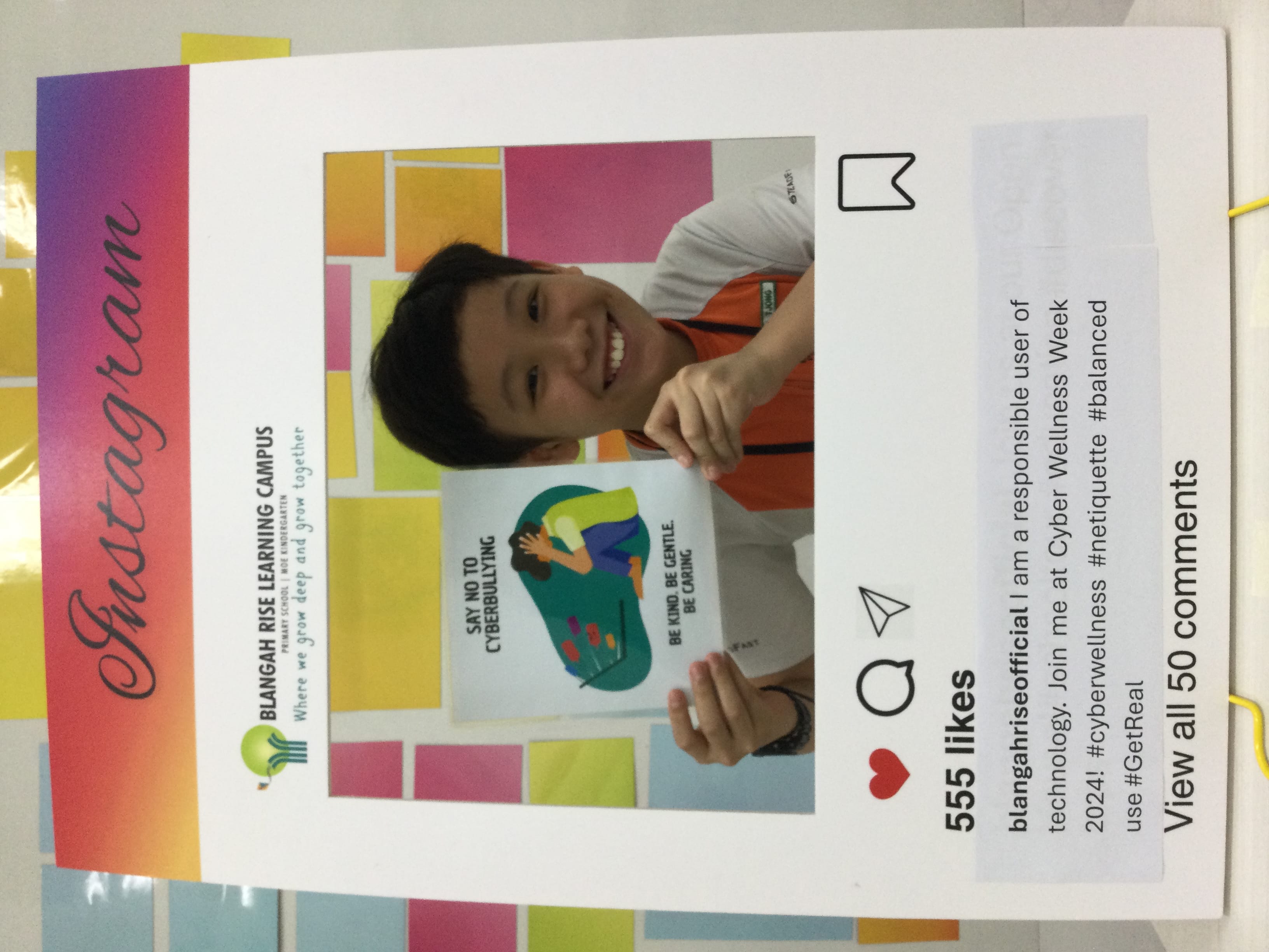 A smiling boy holds a "Say No to Cyberbullying" poster inside a printed Instagram frame from Blangah Rise Learning Campus.