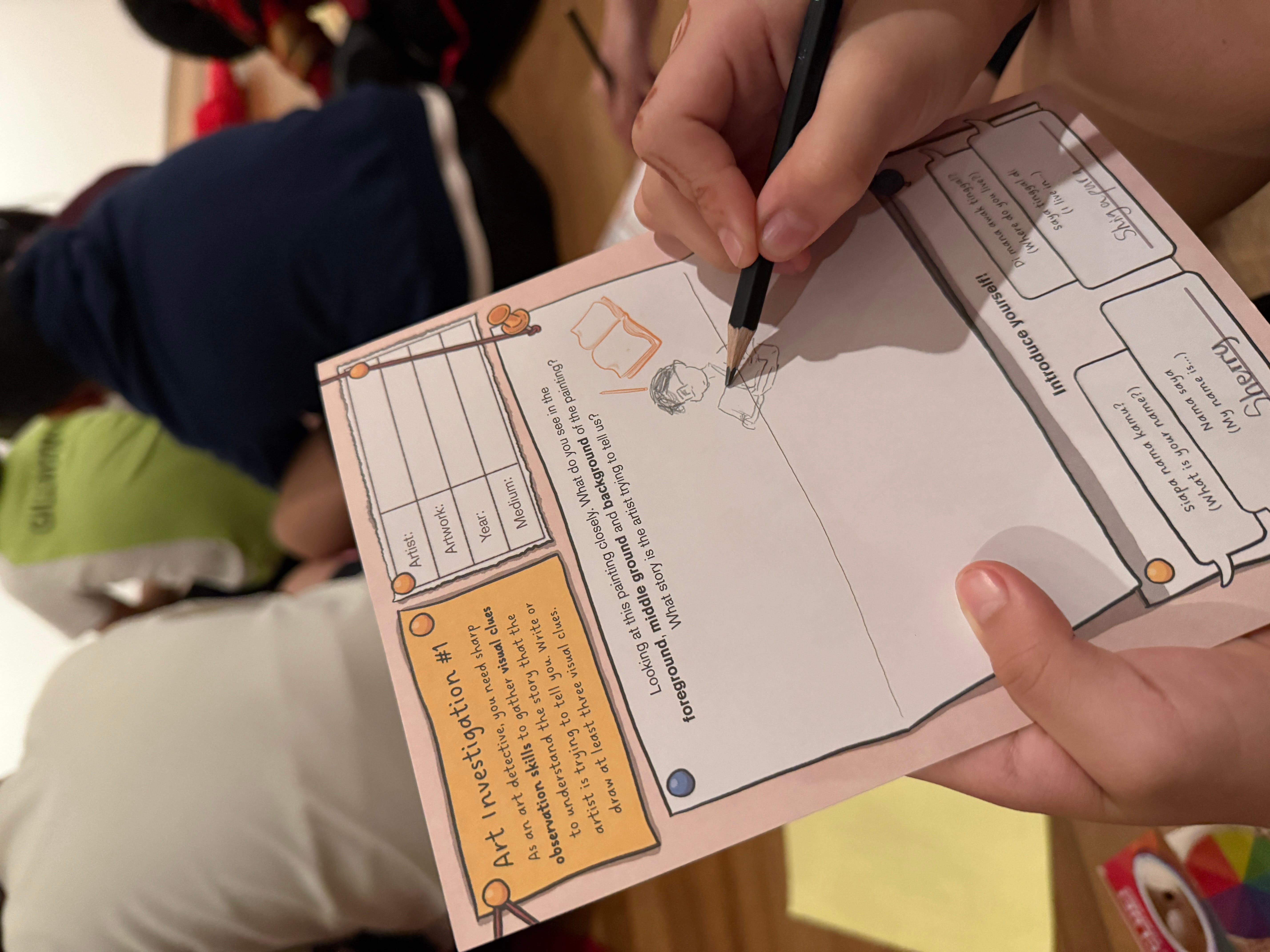 A child holds a pencil over an Art Investigation worksheet with prompts about foreground, middle ground, and background.