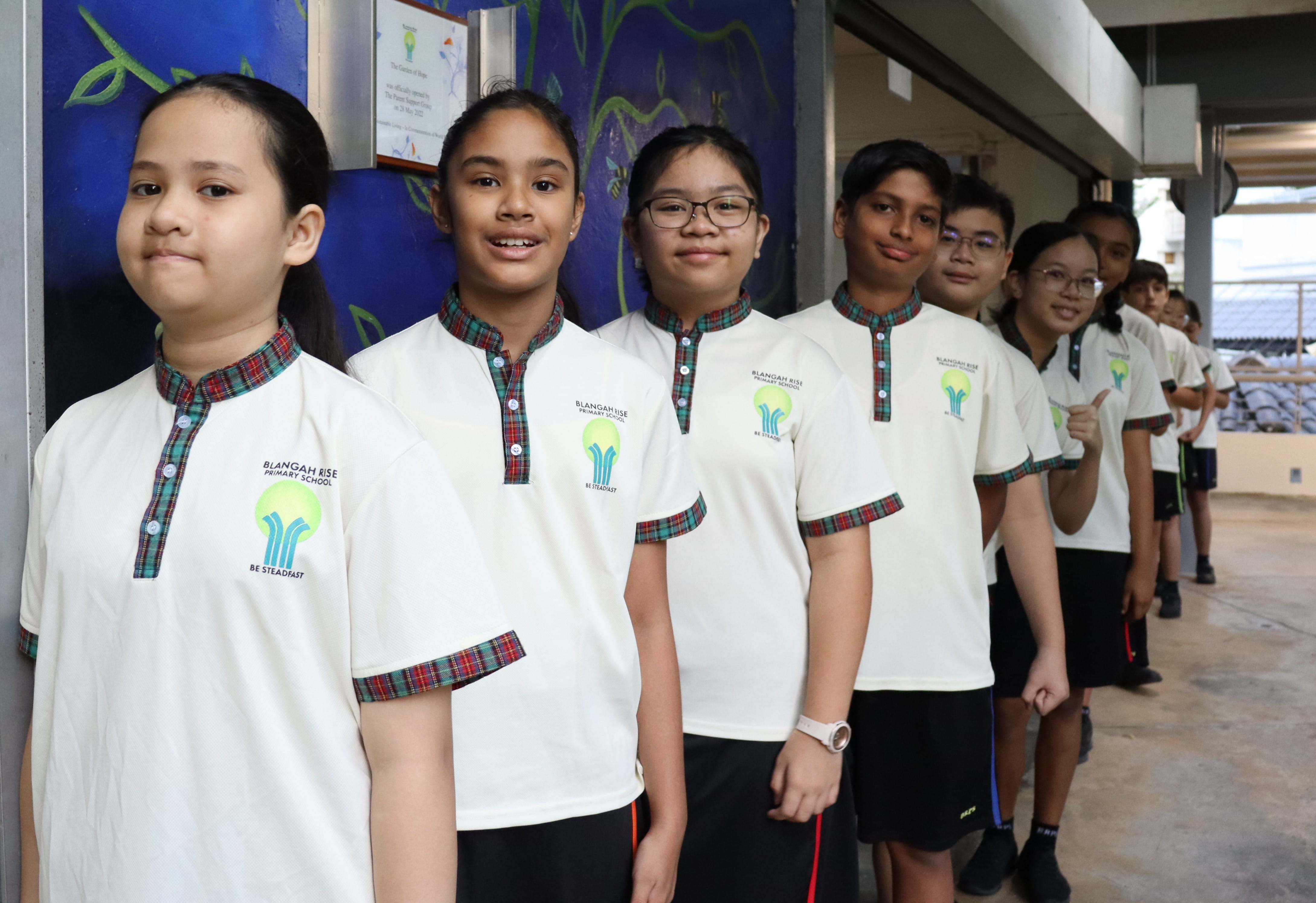 Students in Blangah Rise Primary School uniforms standing in a line outdoors, smiling at the camera.