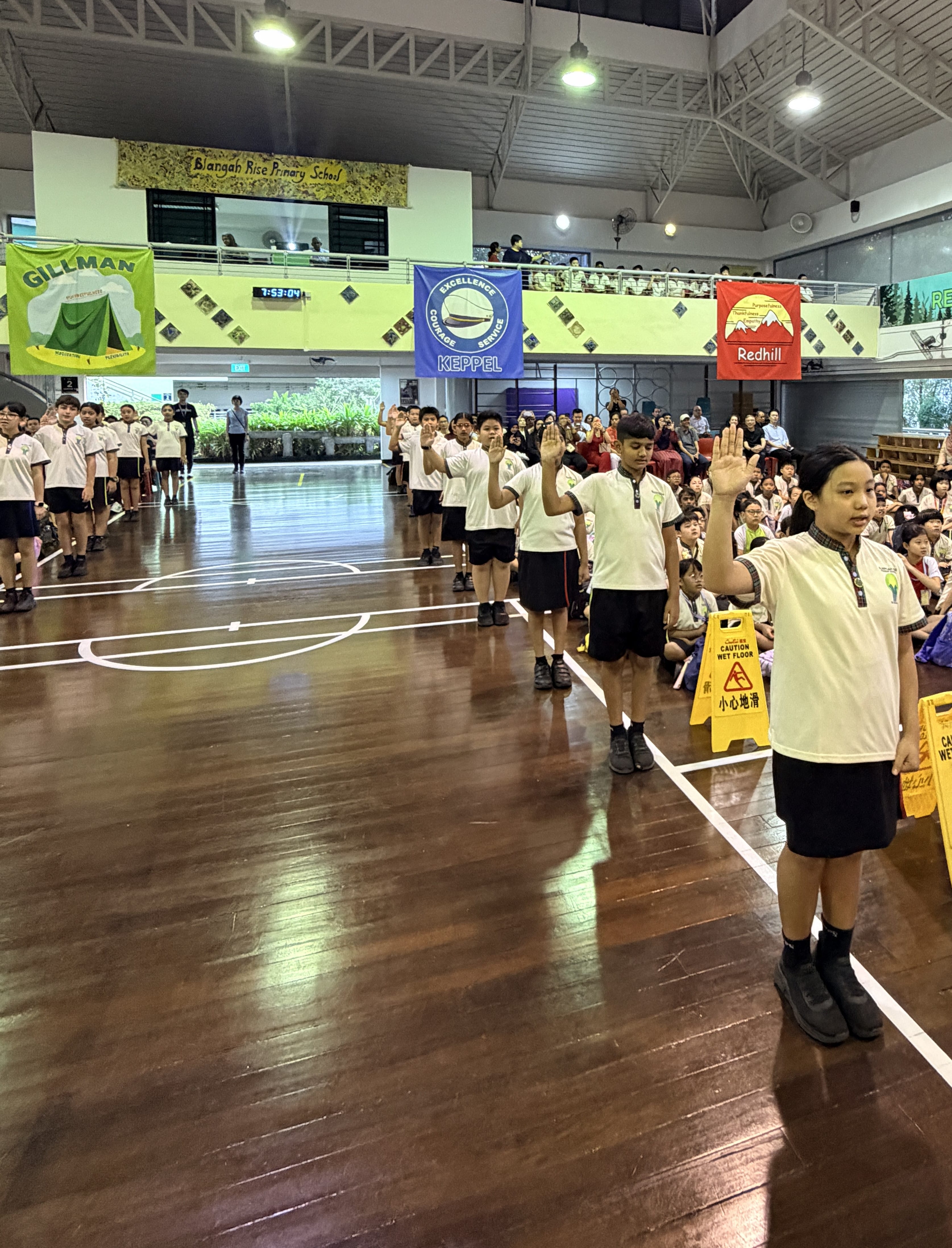Students in white uniforms raise their right hands during a school assembly at Blangah Rise Primary School.