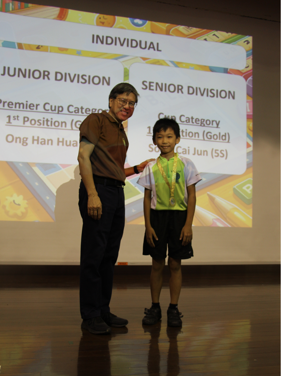 An adult man and a young boy wearing a gold medal stand on a stage before a projected award results slide.