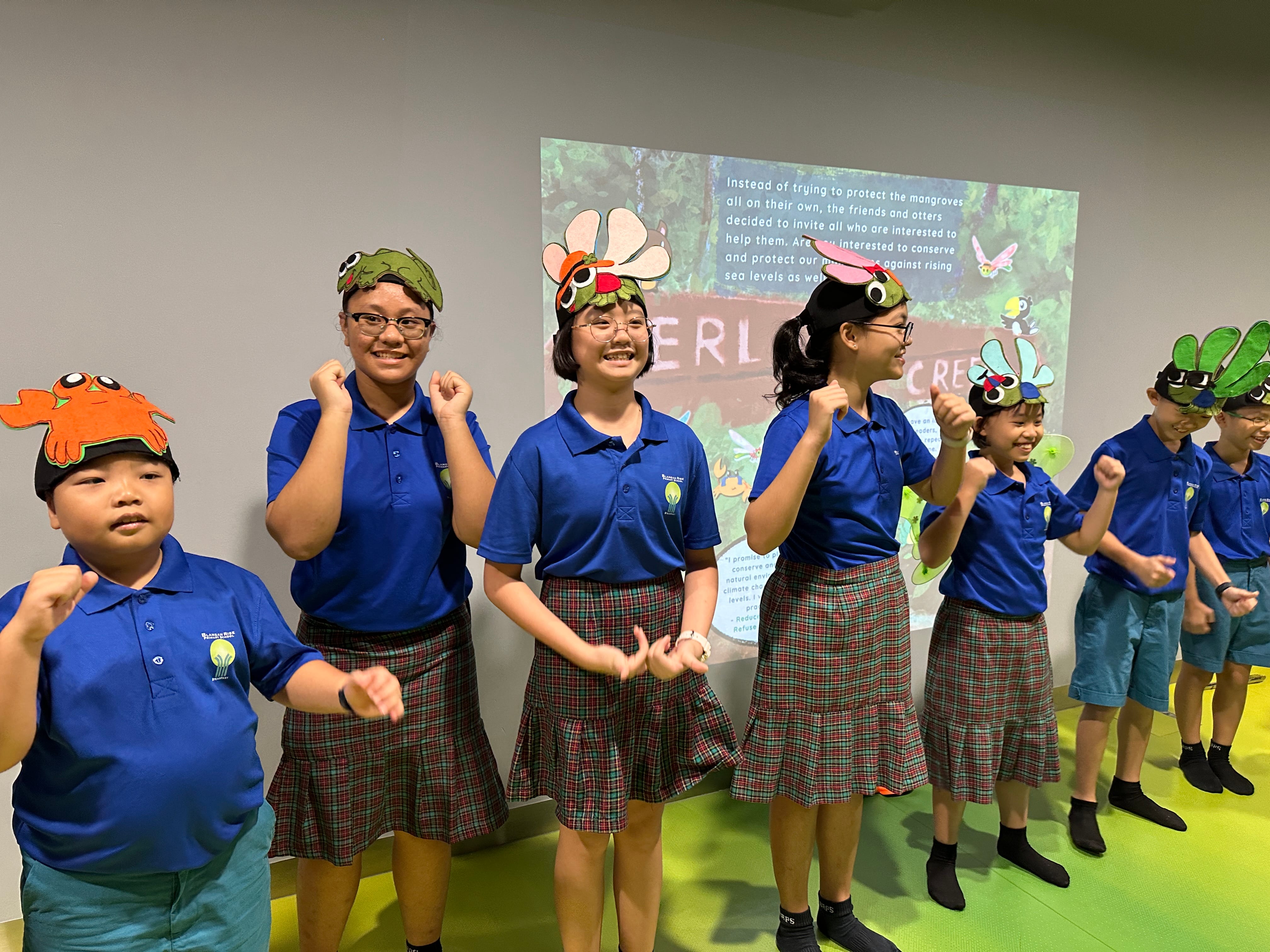 Seven children in blue uniforms wear animal headbands and pose with raised fists in front of a projection.
