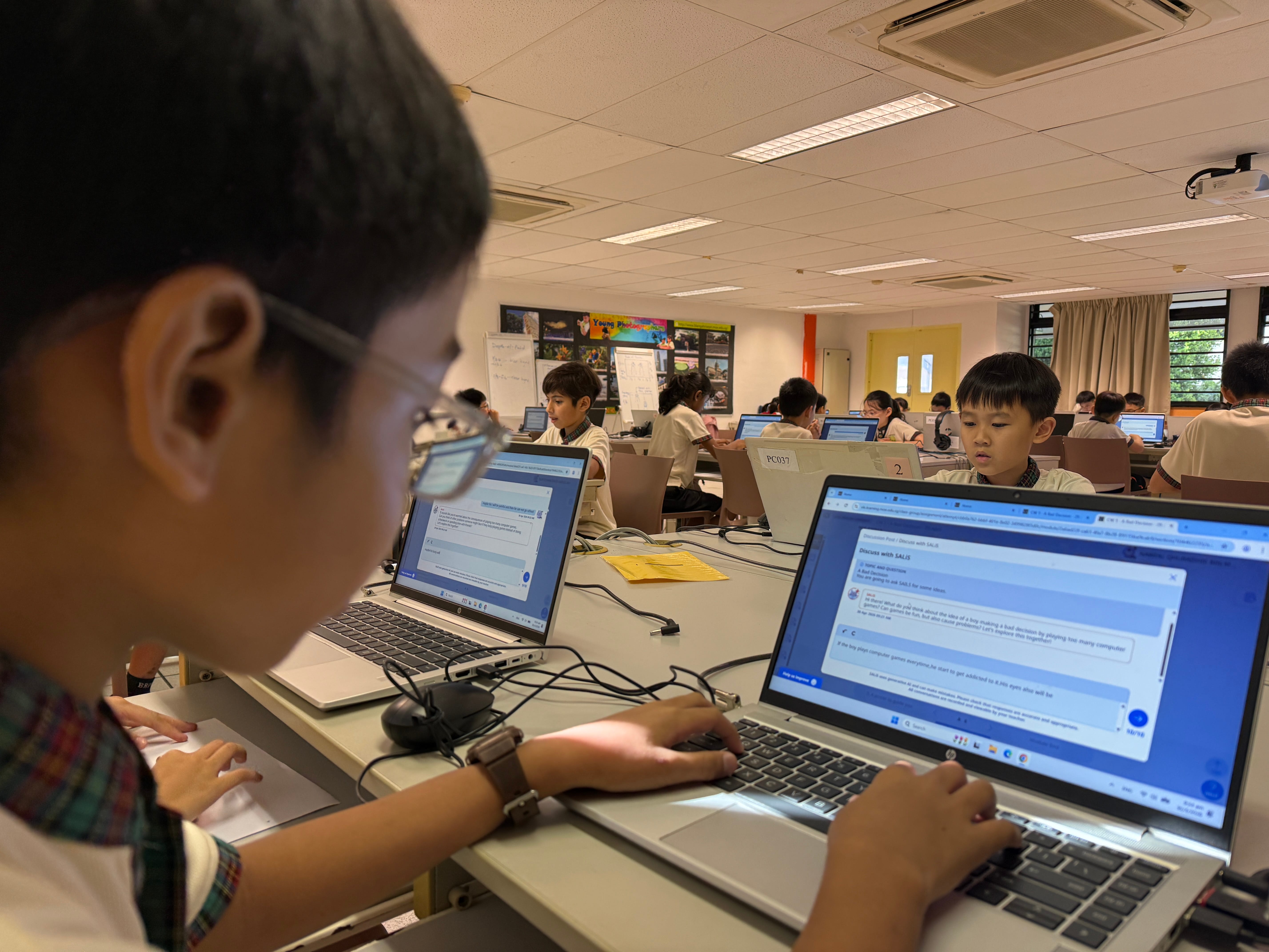 Student in foreground types on a laptop in a classroom where other students work at laptops.