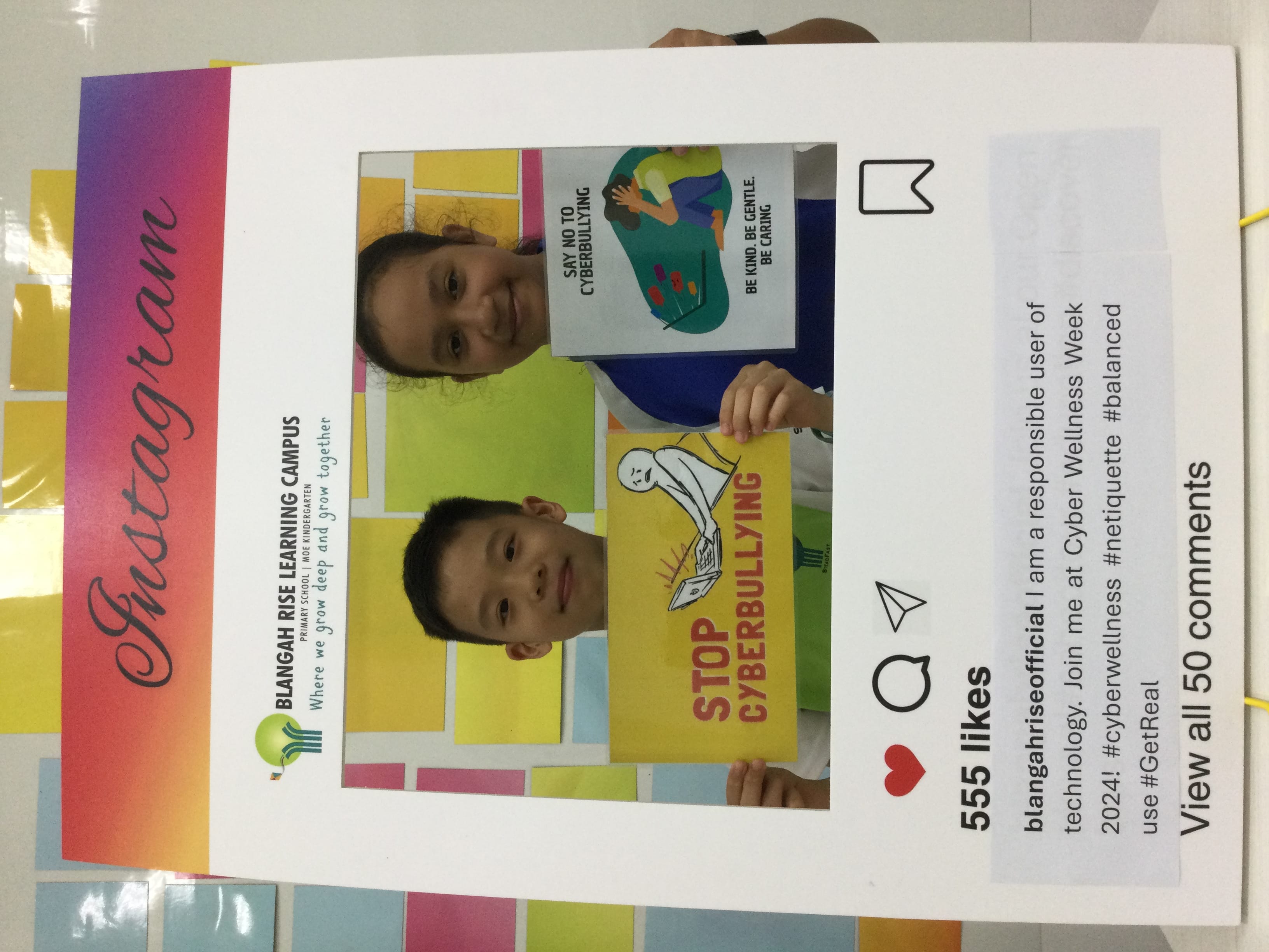 Two children hold anti-cyberbullying signs inside a cardboard Instagram frame from Blangah Rise Learning Campus.