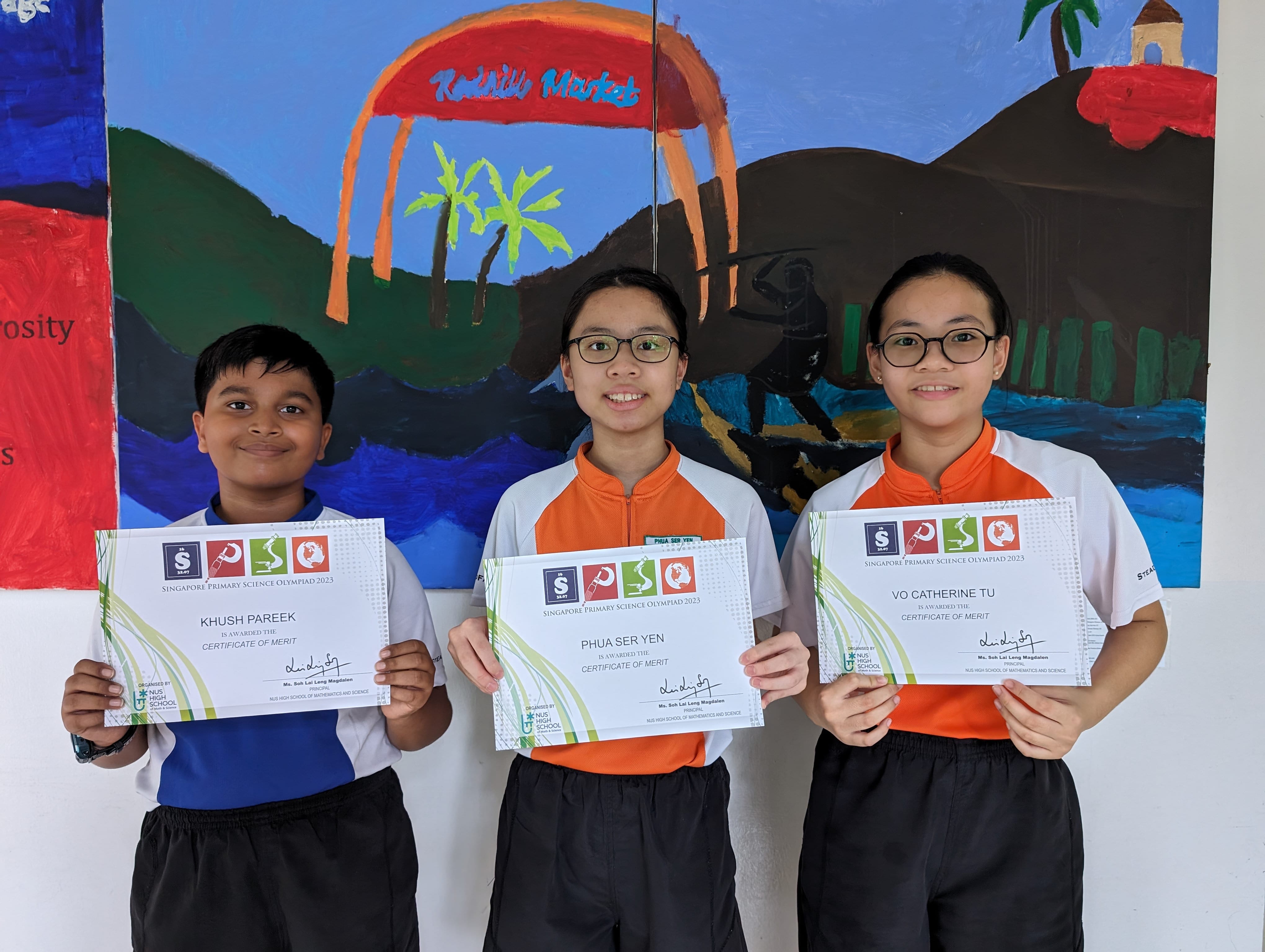 Three students smile holding Singapore Primary Science Olympiad 2023 Certificates of Merit in front of a colorful mural.