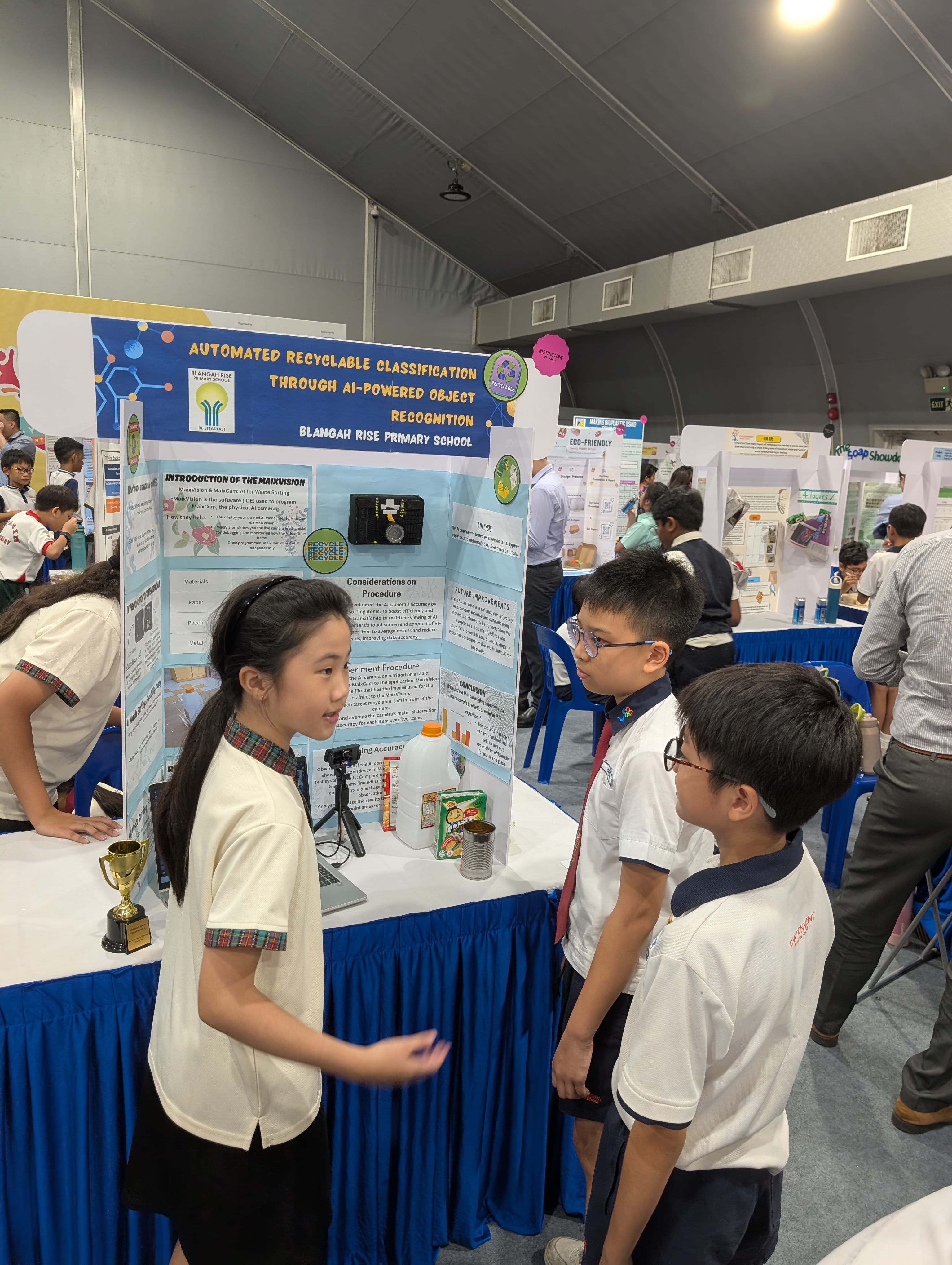 Three primary school students present a science fair project on AI-powered recyclable classification at Blangah Rise Primary School.