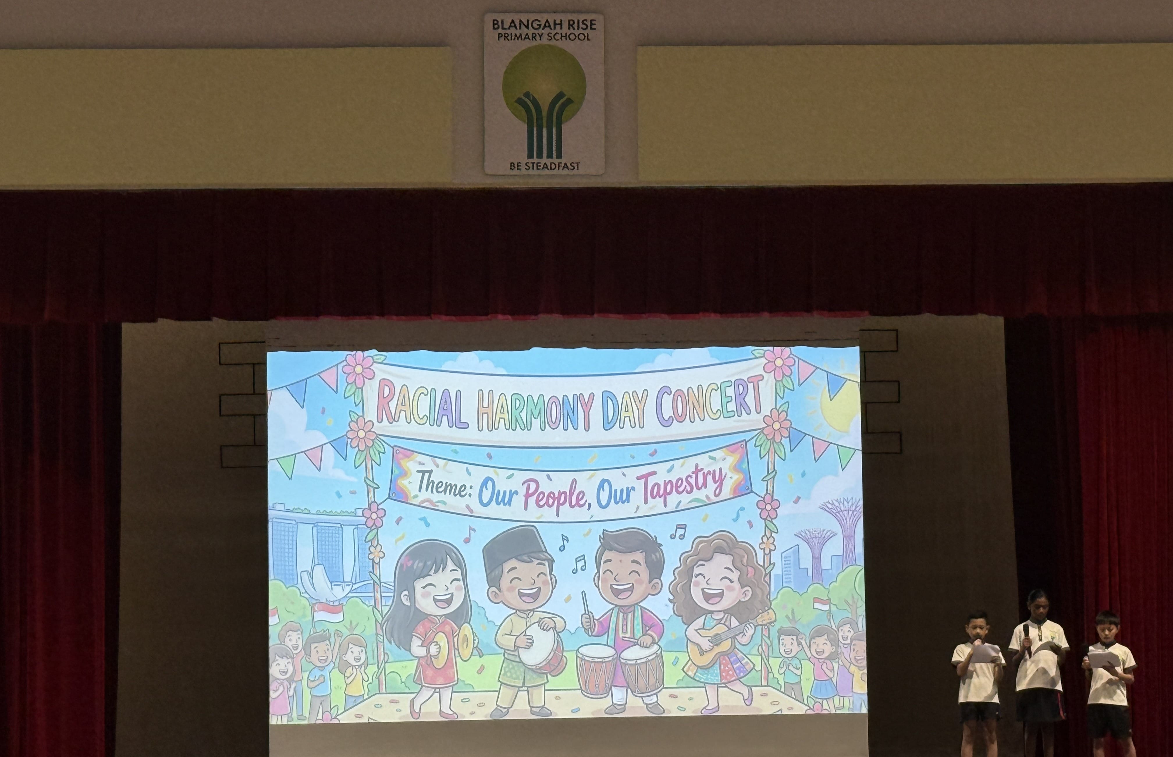 Blangah Rise Primary School stage with a projected slide reading Racial Harmony Day Concert, theme Our People Our Tapestry.