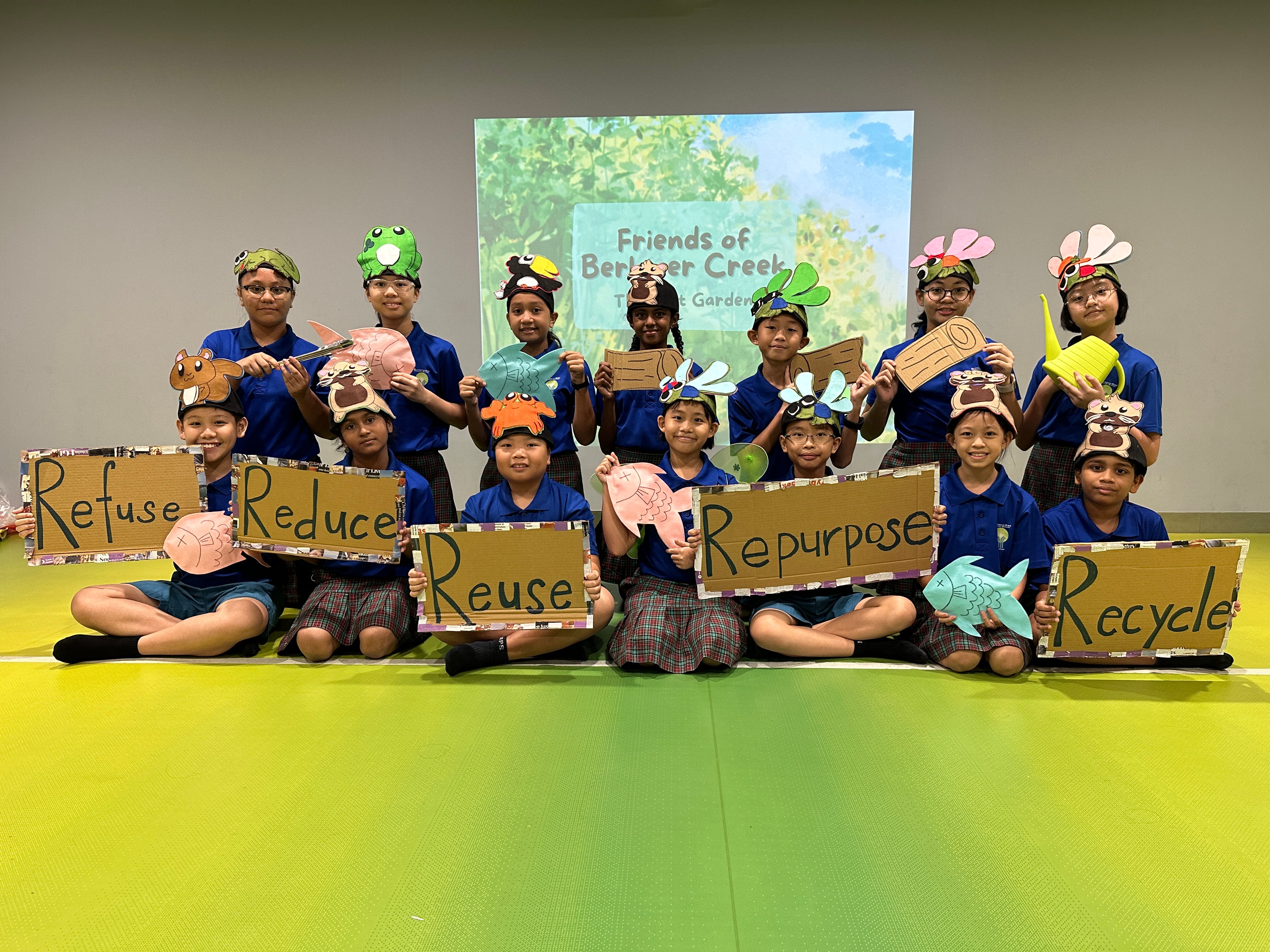 Group of kids in blue shirts hold signs: Refuse, Reduce, Reuse, Repurpose, Recycle, wearing animal hats.