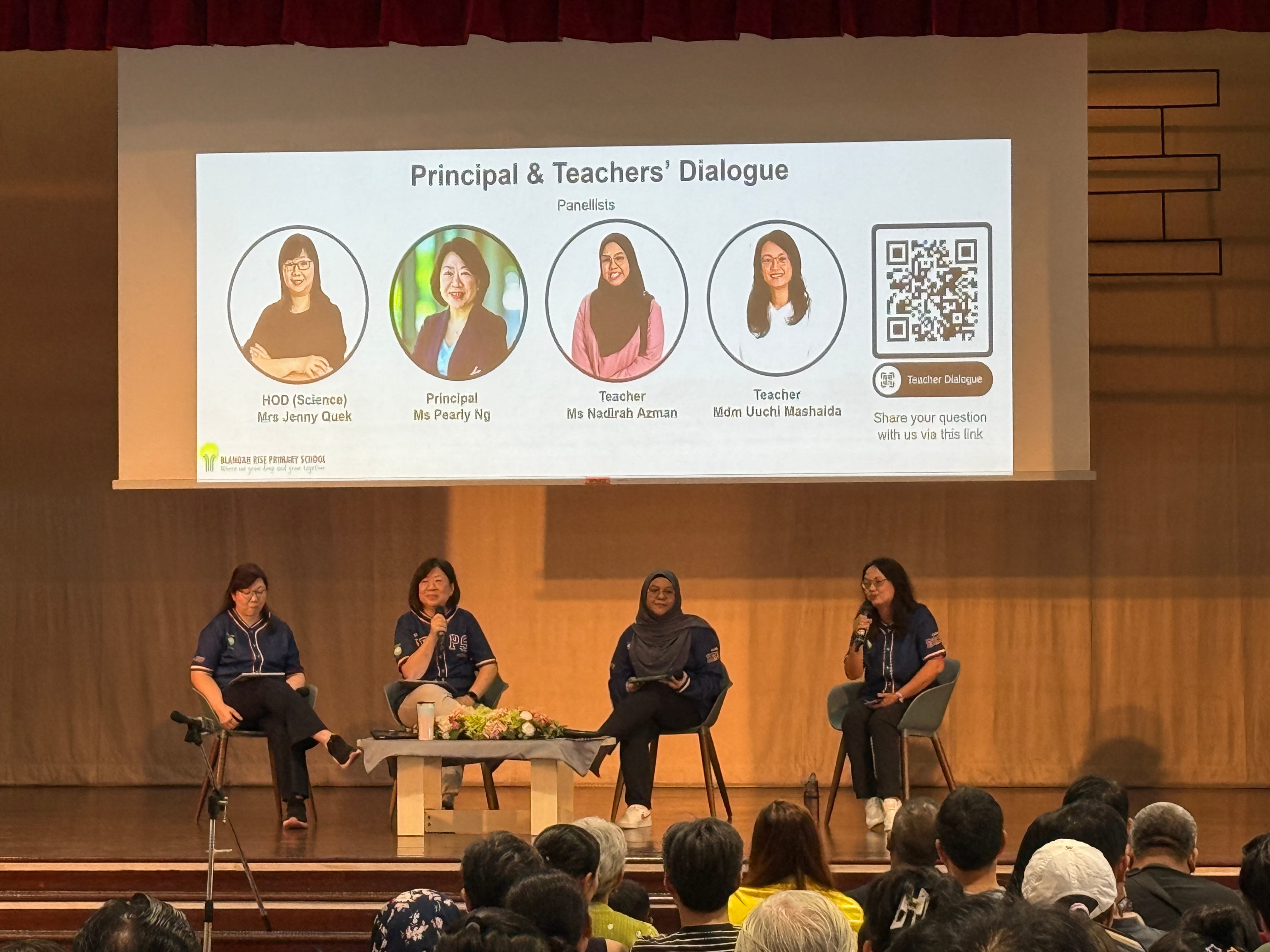 Four women sit on stage for a Principal and Teachers Dialogue at Blangah Rise Primary School before an audience.