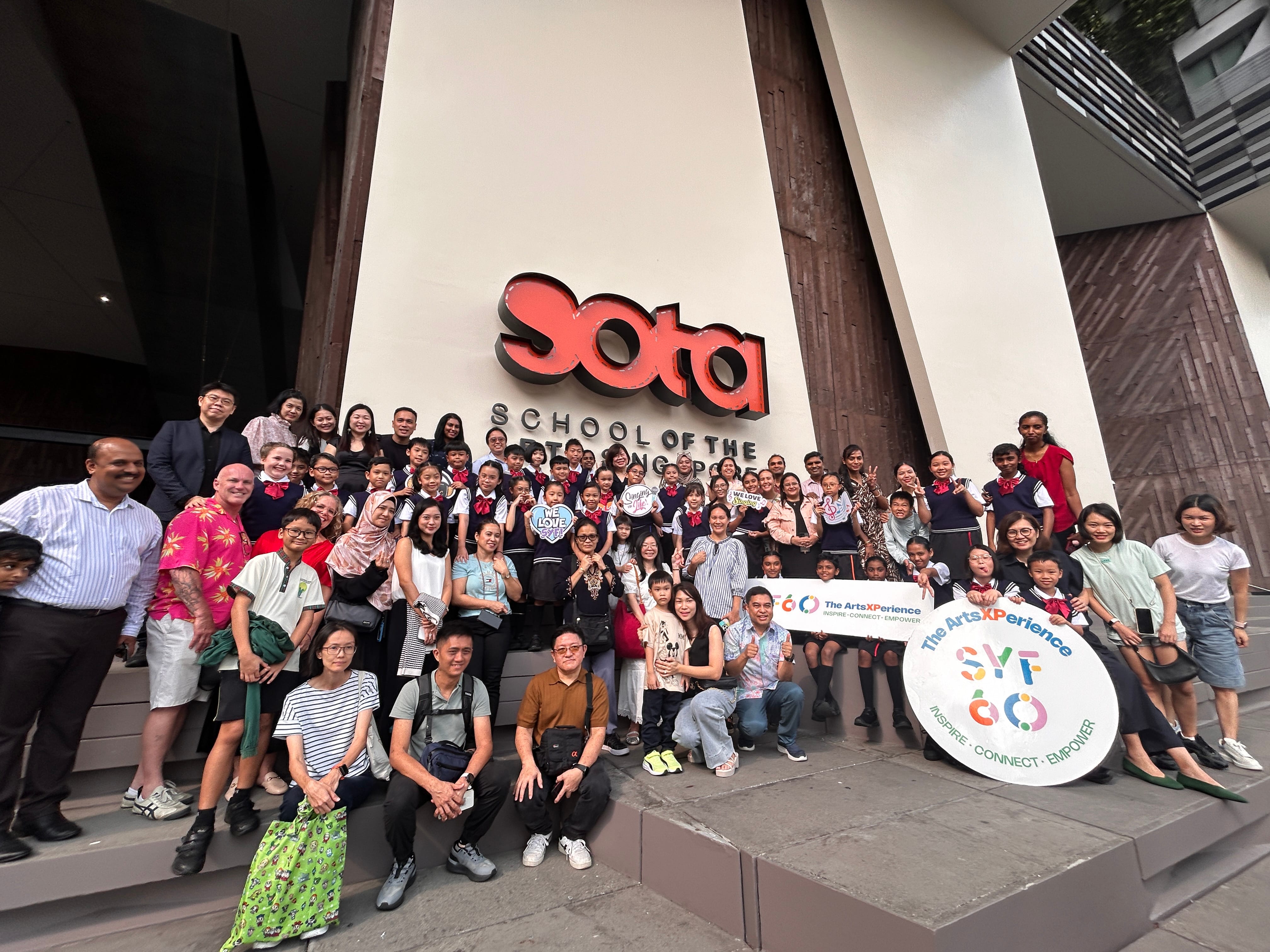 Large group of adults and uniformed children posing on steps in front of the SOTA School of the Arts Singapore sign.