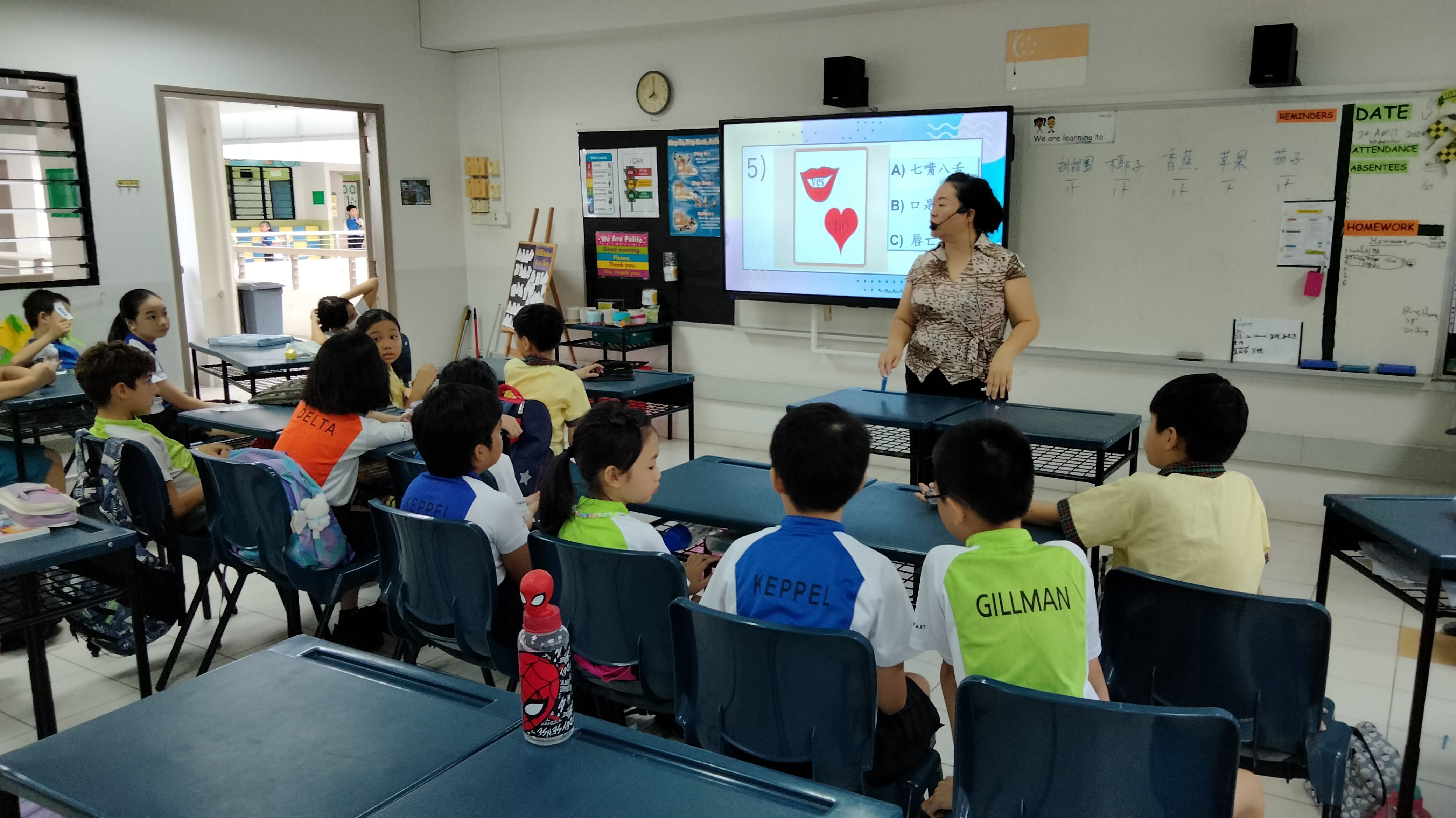 A teacher stands at the front of a classroom with students at desks, presenting a Chinese lesson on a large screen.