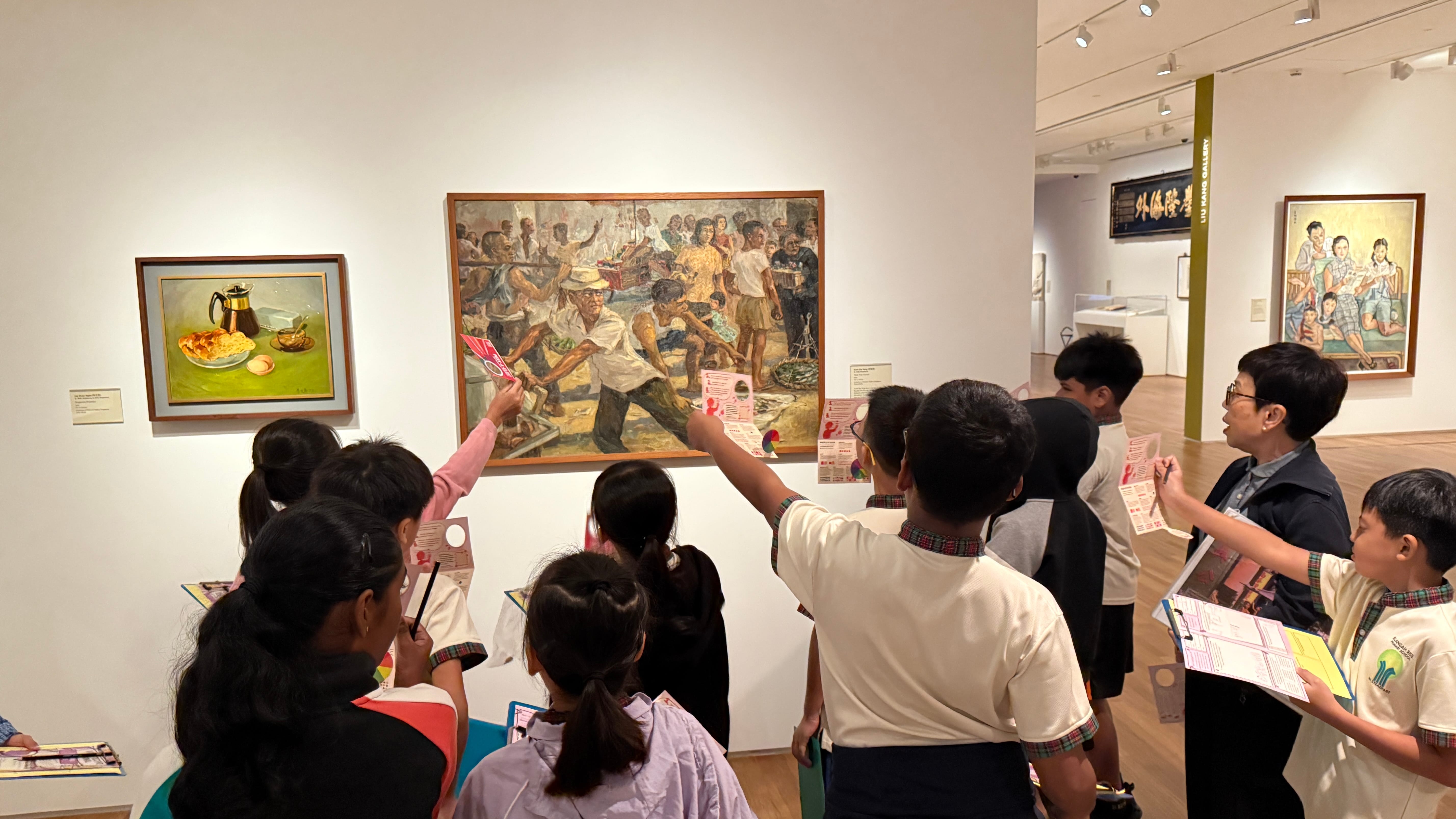 A group of school children holding worksheets view paintings on white gallery walls during a guided museum tour.