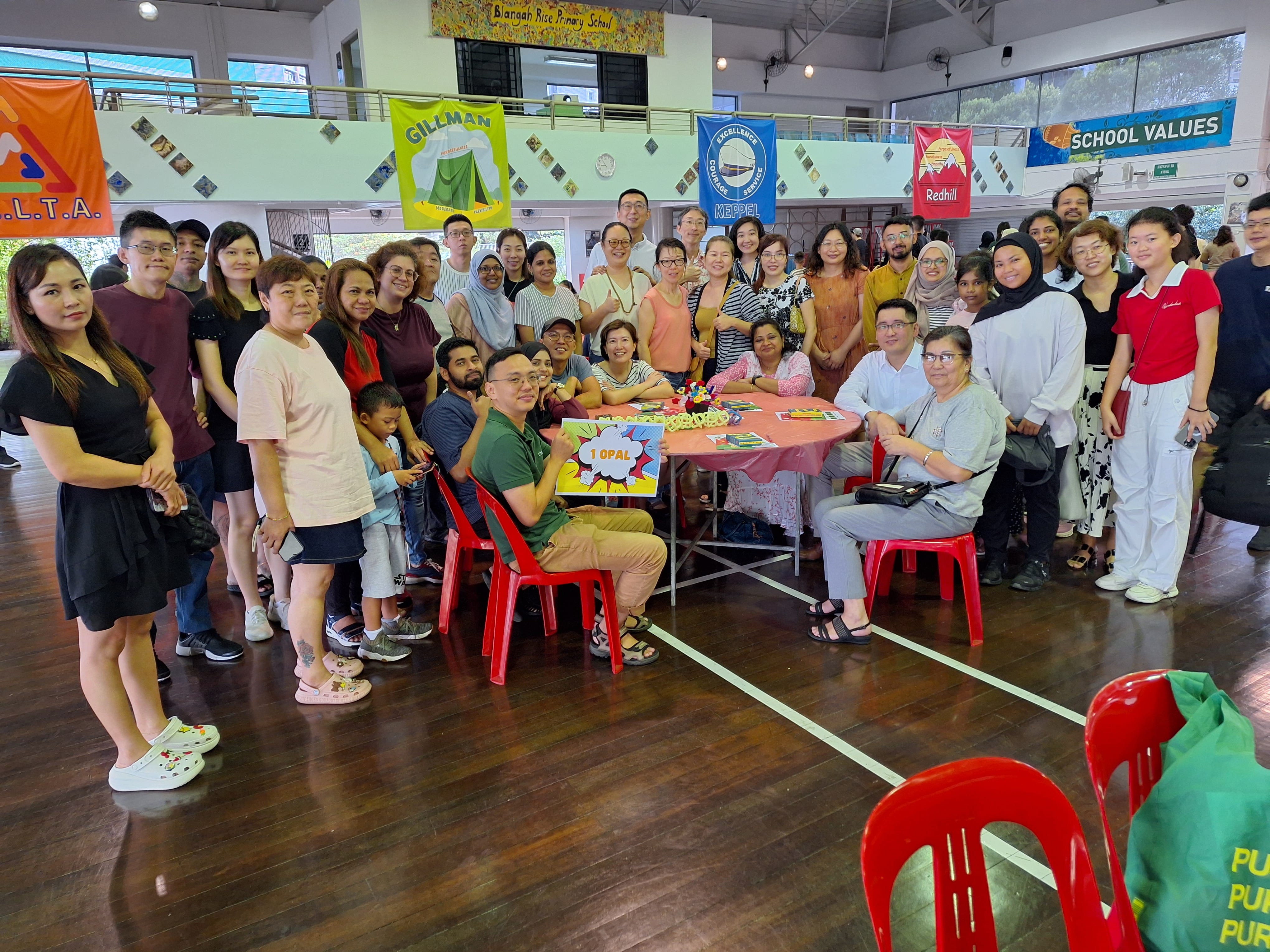 Large group posing around a table with craft items in a school hall with colorful banners overhead