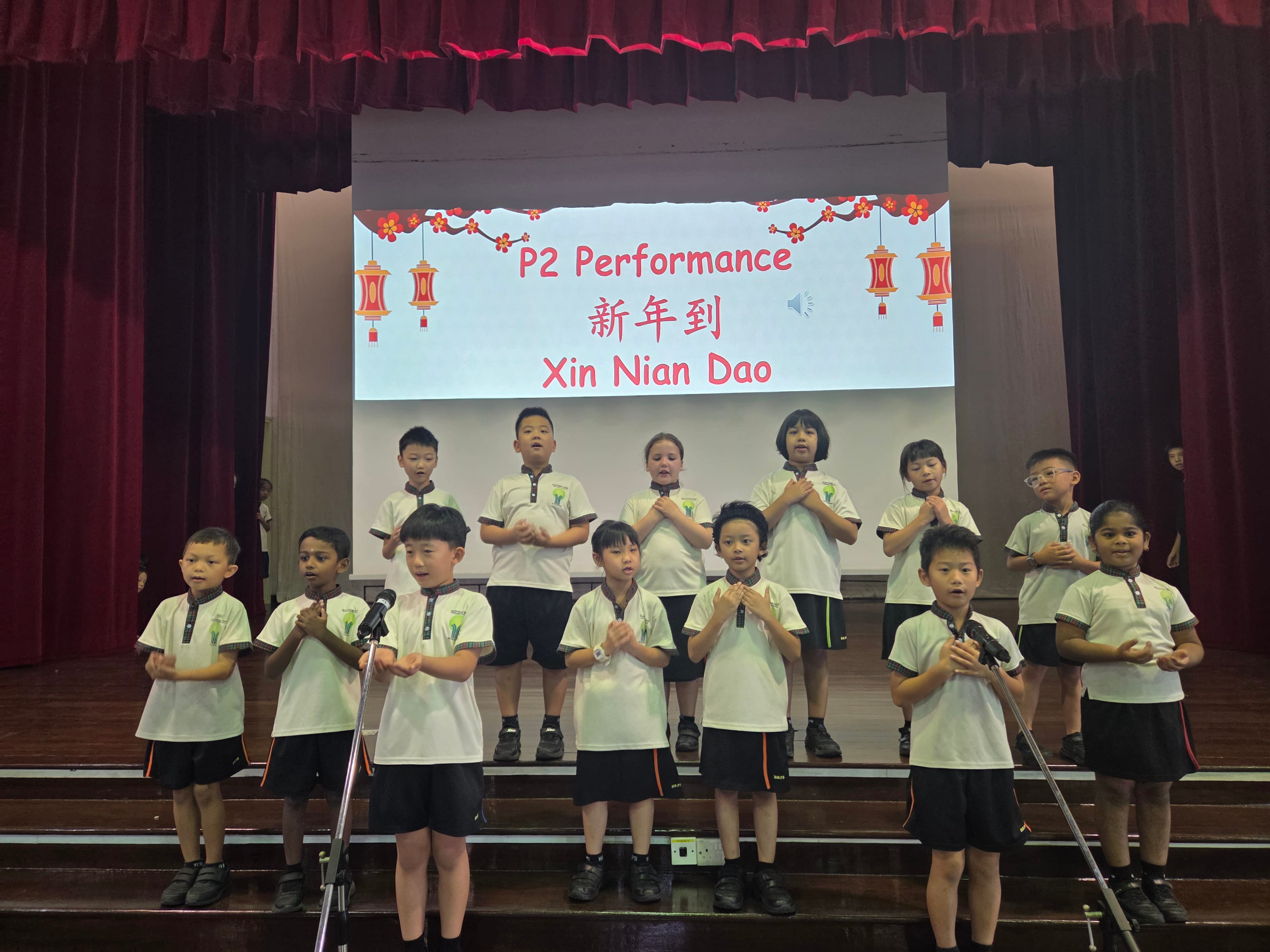 Young students in white uniforms perform on stage for a P2 Chinese New Year show titled Xin Nian Dao.