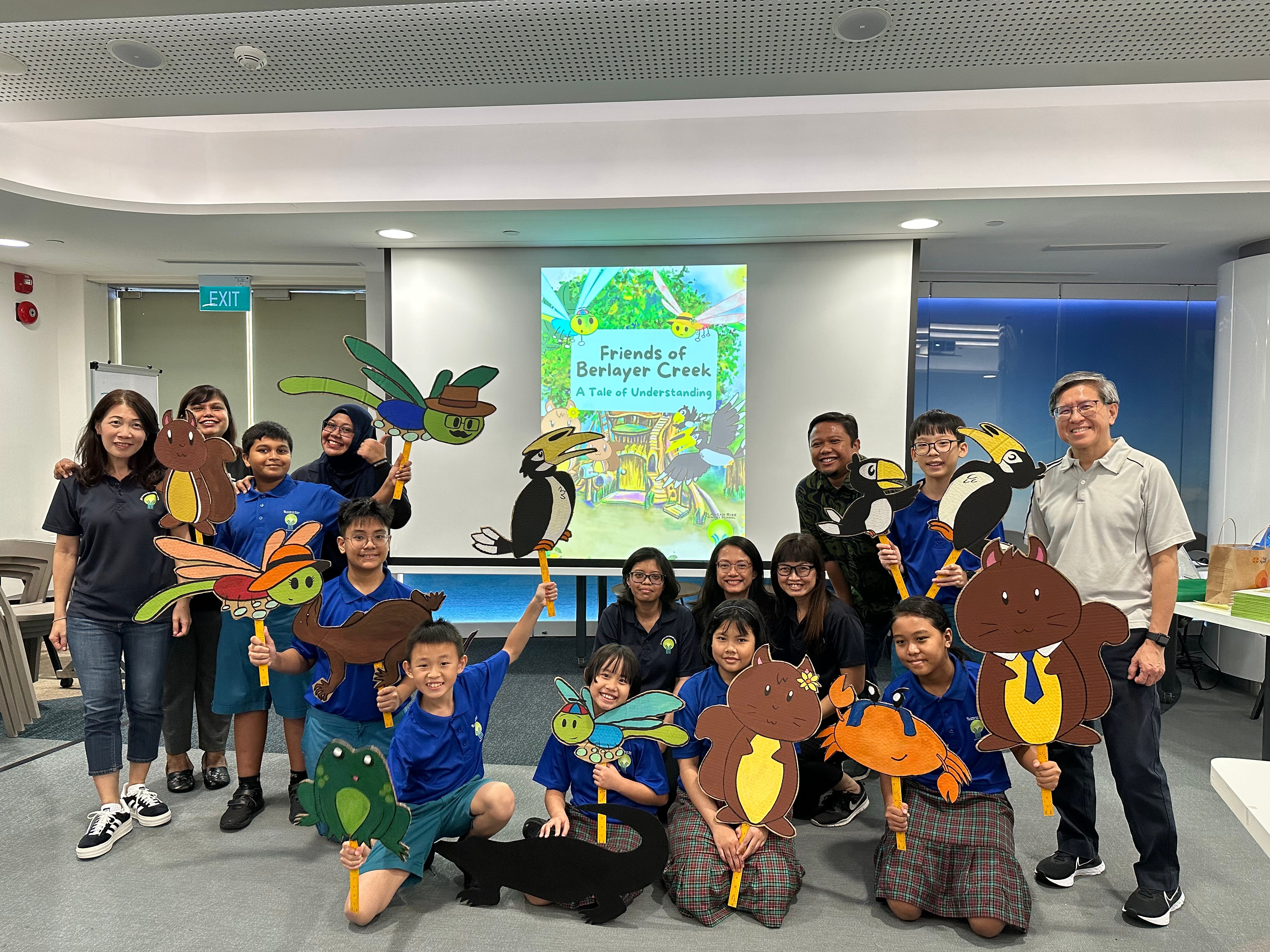 Group of students and adults holding animal cutouts in a classroom; projector shows Friends of Berlayer Creek.