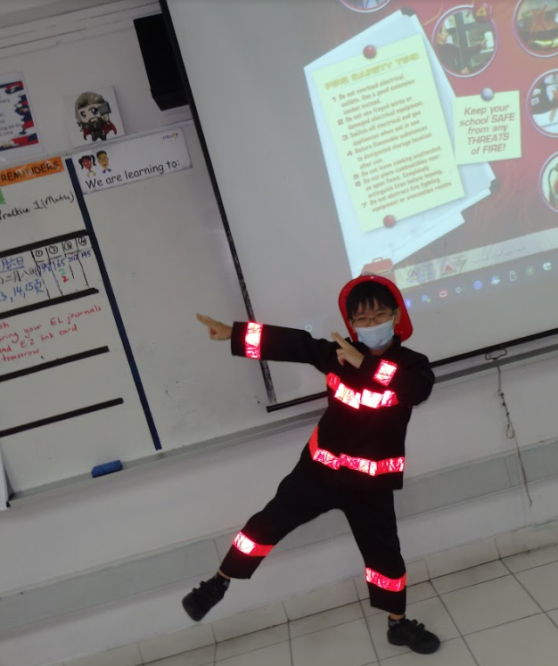 Child in reflective firefighter costume and mask poses in a classroom, projector screen behind.