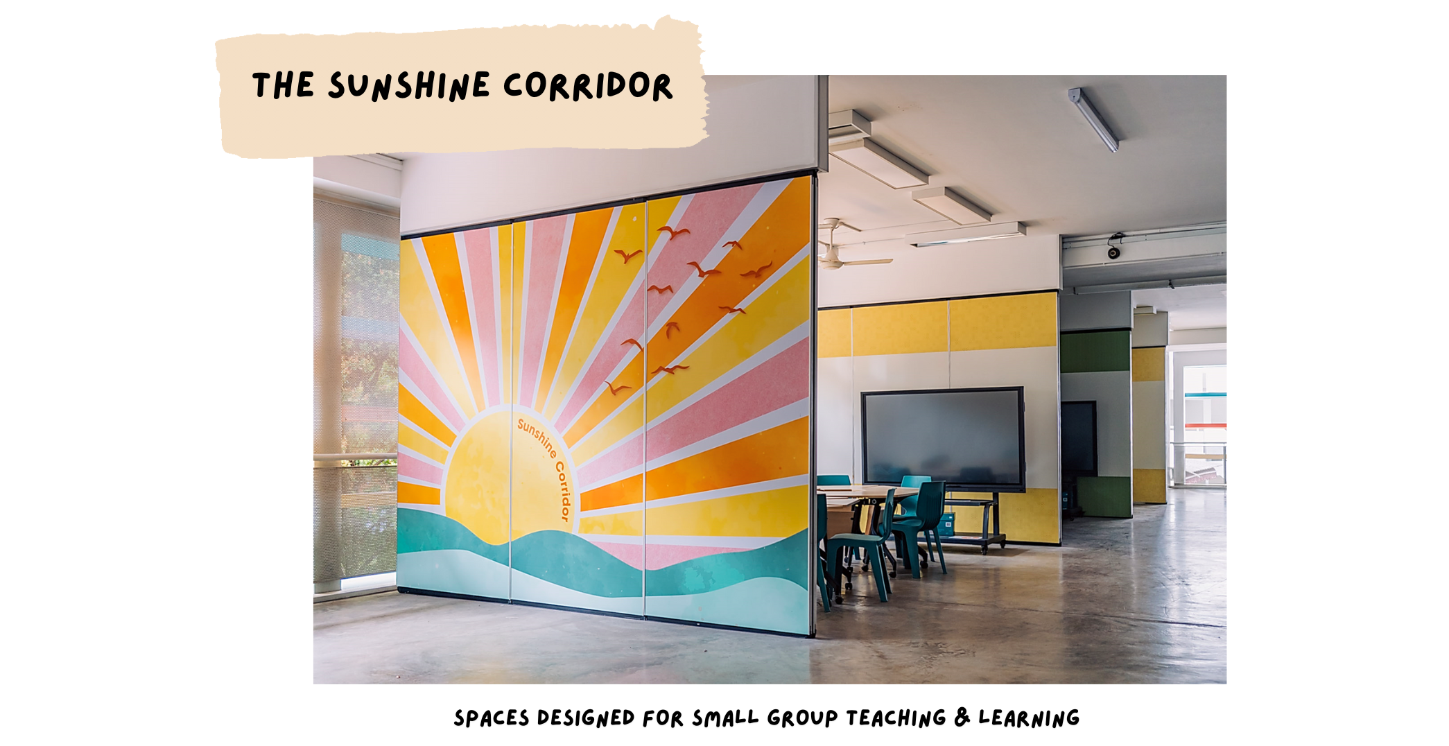 A school corridor with a colorful sun mural on sliding panels, small tables, chairs, and a wall-mounted screen nearby.