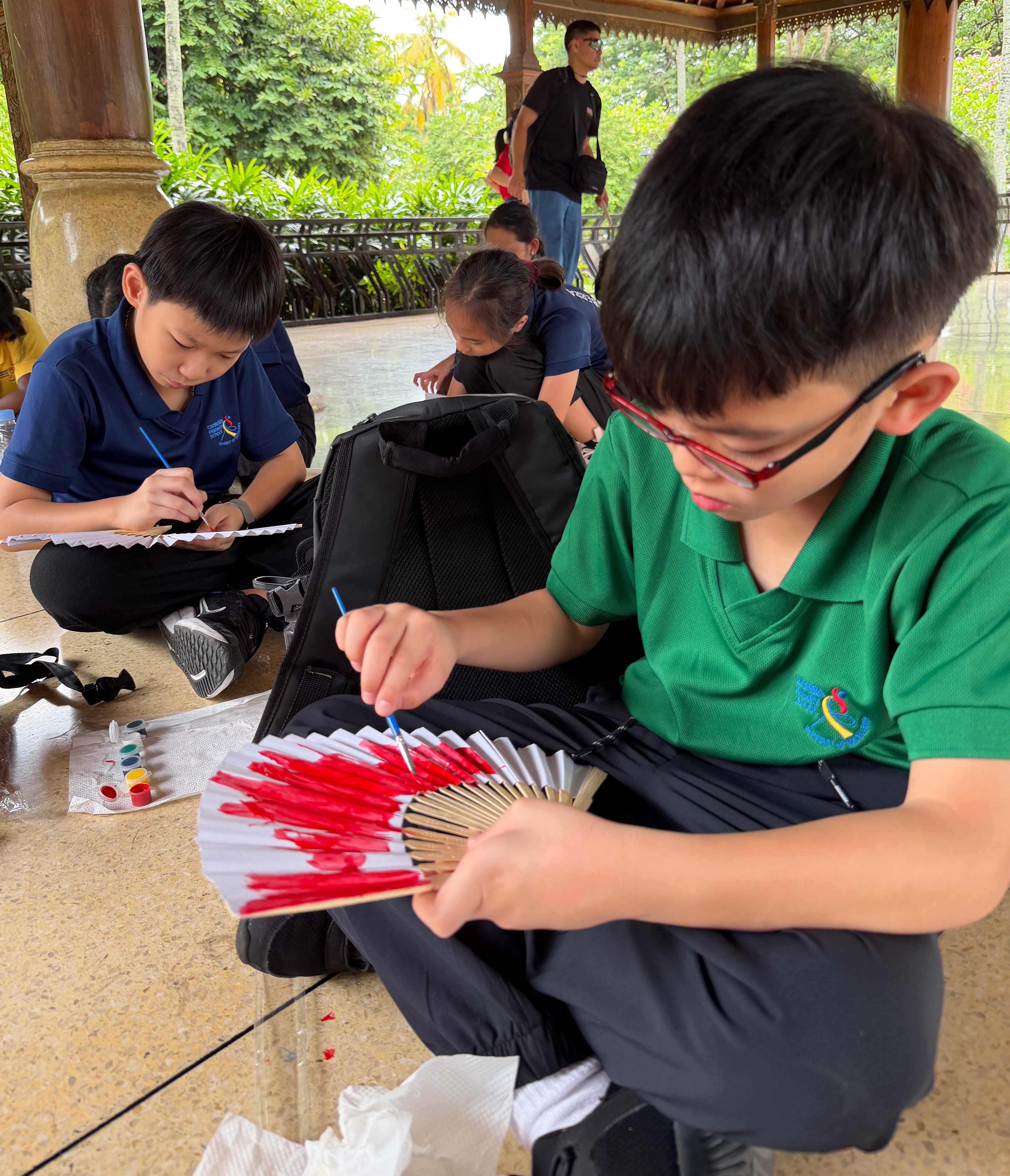 Students painting traditional folding fans during a cultural activity at Taman Mini Indonesia Indah. 